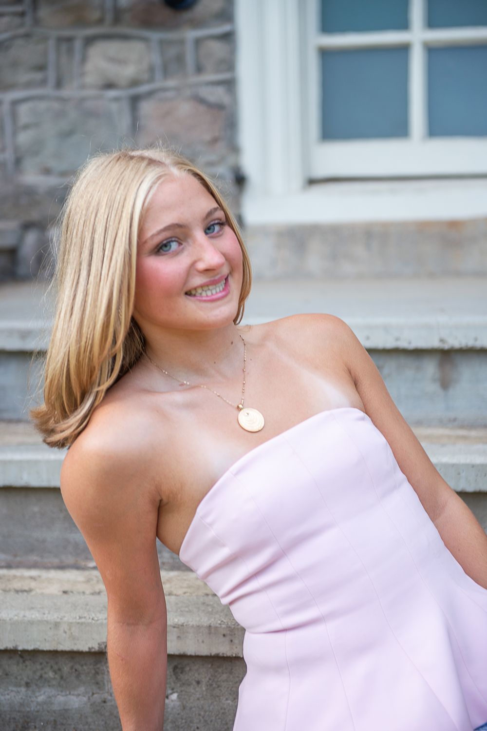Person in pink strapless dress poses on stone steps outdoors with a delicate necklace.