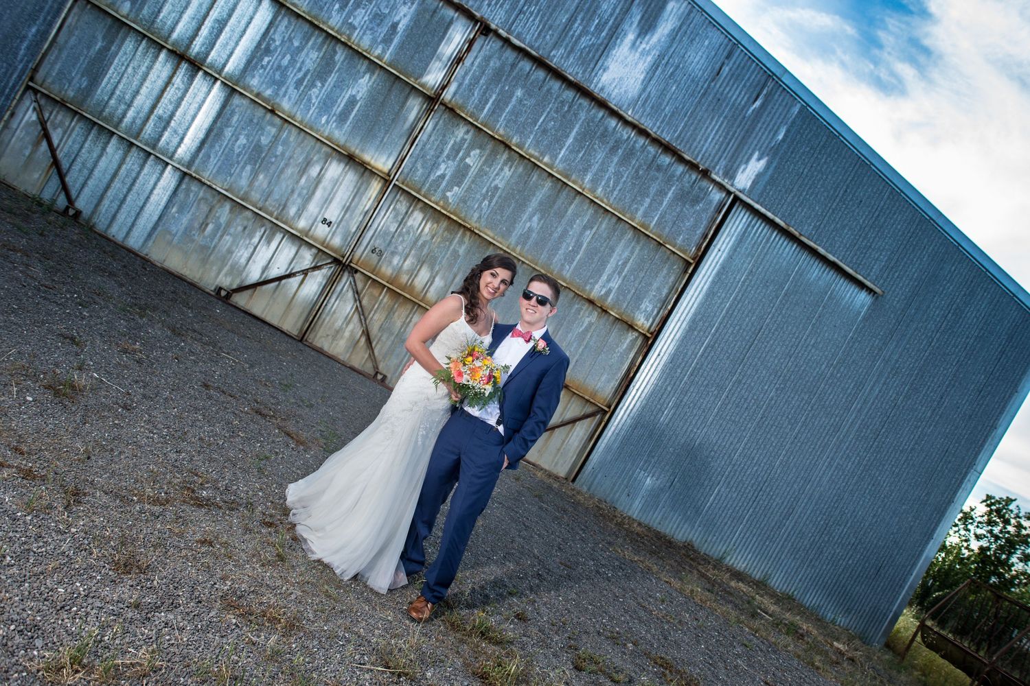 A couple poses together in front of a rustic metal wall in an industrial setting on their wedding day.