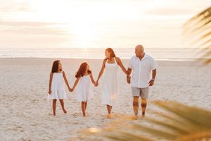 A family walks hand in hand along a sandy beach at sunset creating silhouettes against the golden sky.