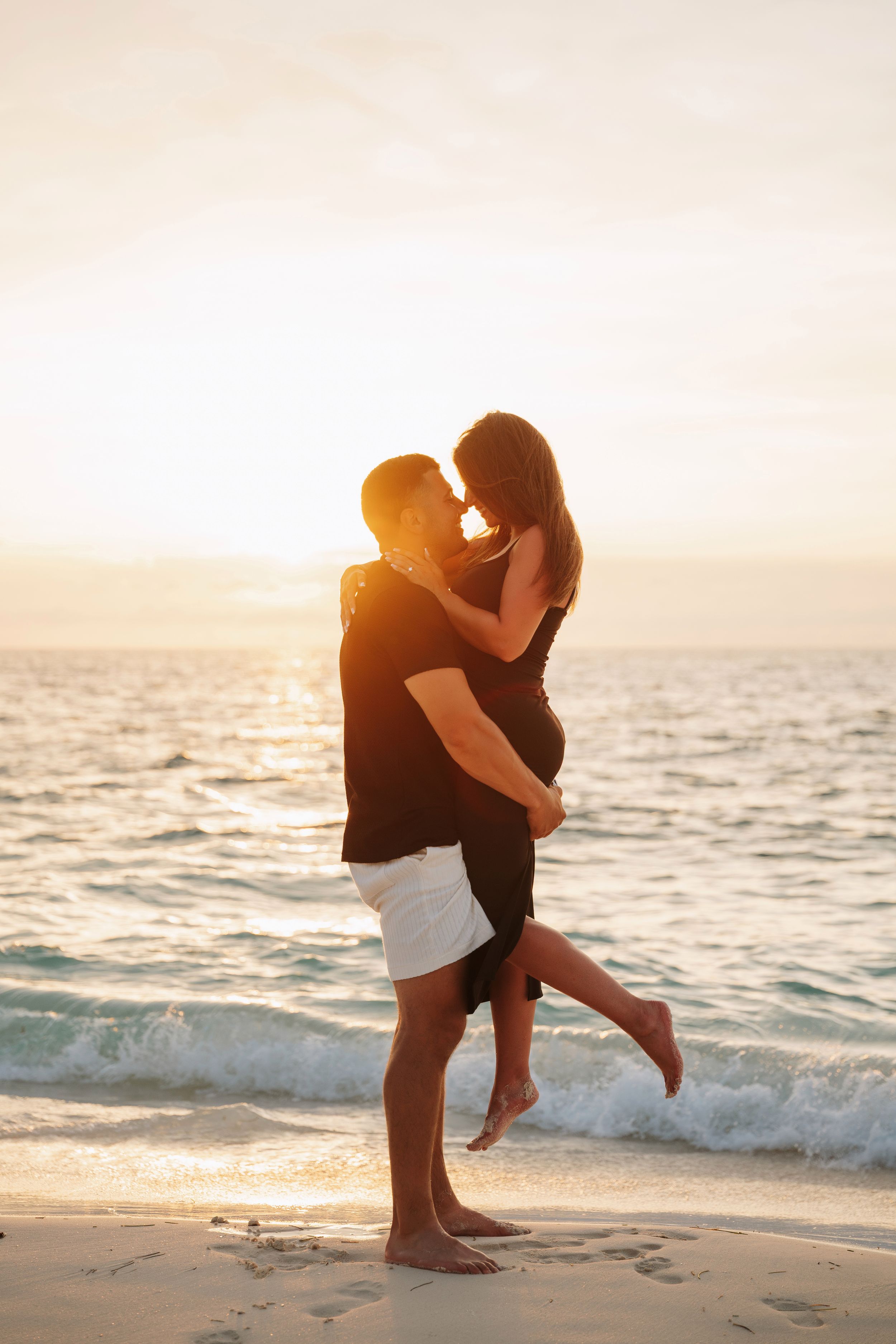 Silhouettes of two people embracing on a beach at sunset with waves crashing in the background.