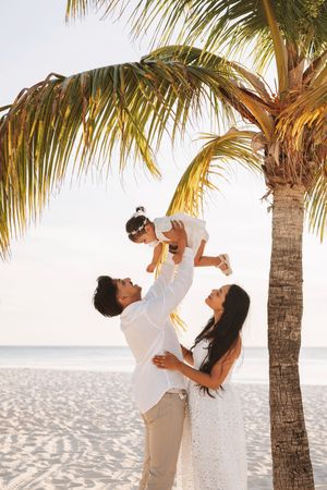 A couple in white clothing shares tender moments under palm trees on a tropical beach at sunset.