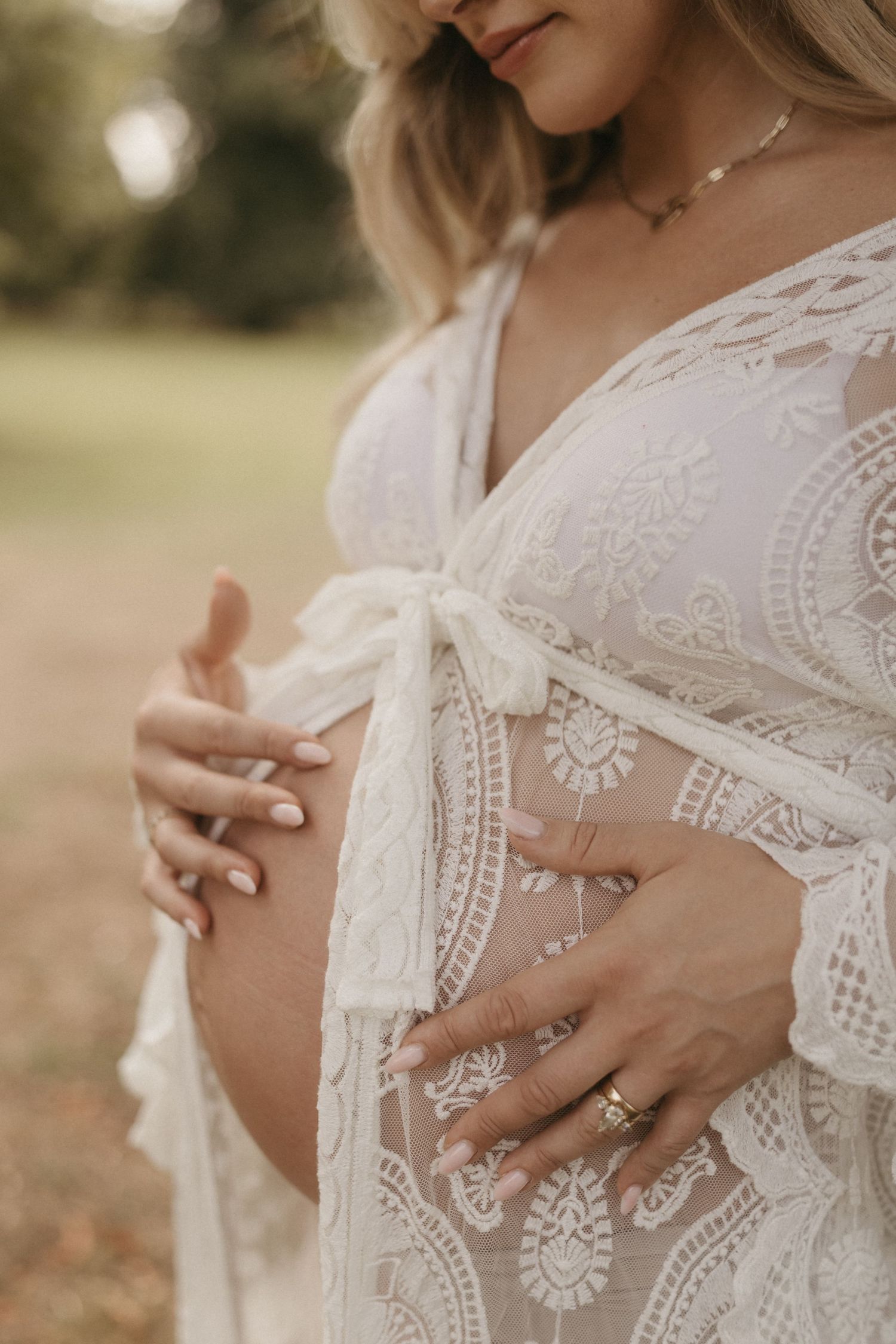 Close-up details of delicate white lace wedding dress with intricate embroidery patterns and a ring-adorned hand.
