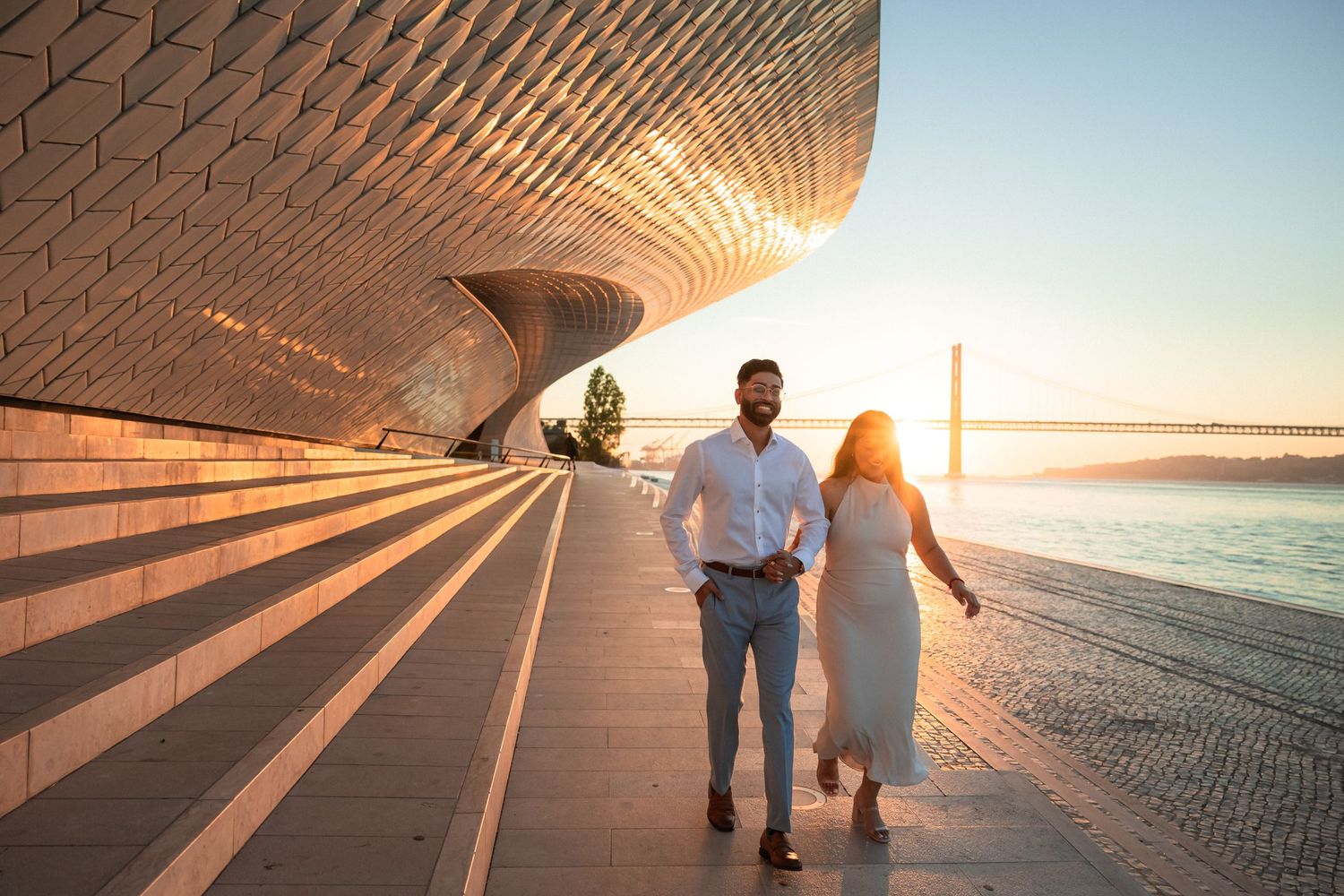 Cinematic sunrise engagement session at MAAT Lisbon — couple walking by the river, captured by destination wedding photographer in Portugal
