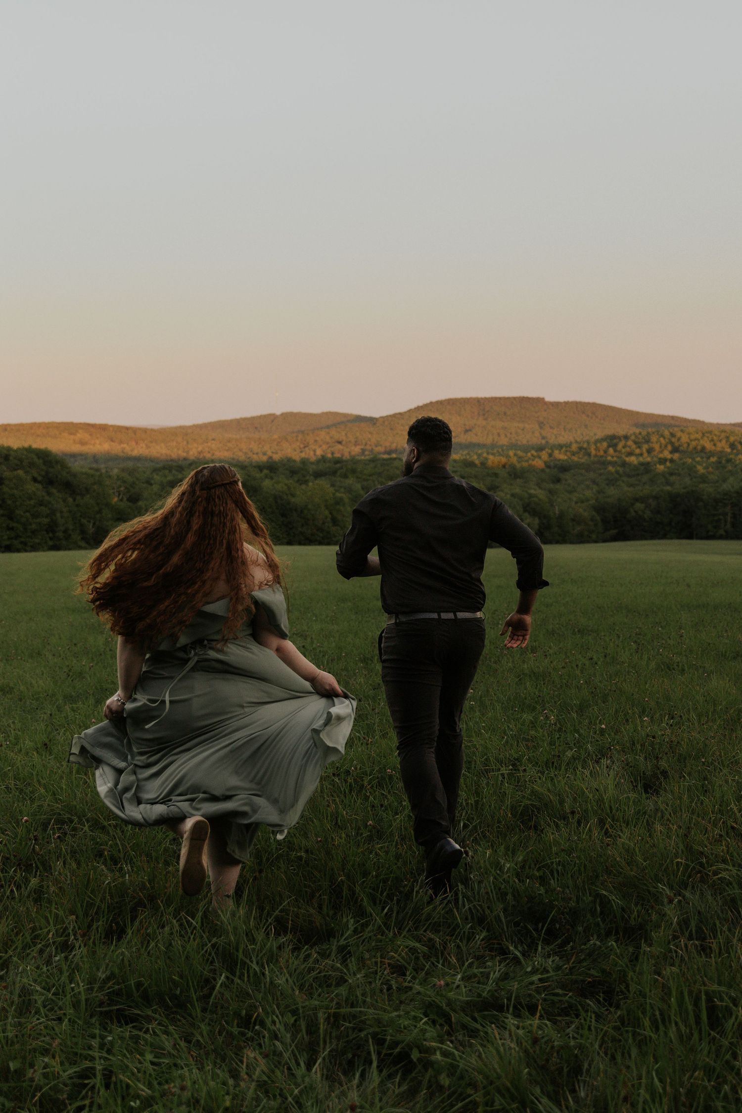 People running through a grassy field at dusk with mountains in the background.