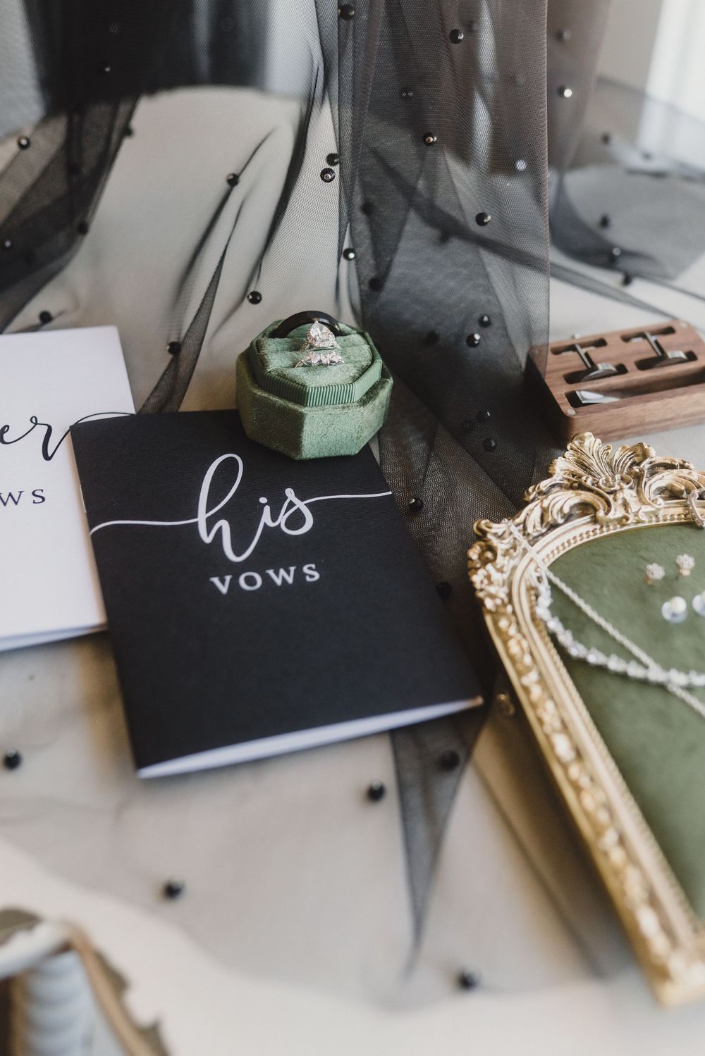 Wedding vows books in black and white with decorative gold frame and mint green trinket box on light surface.