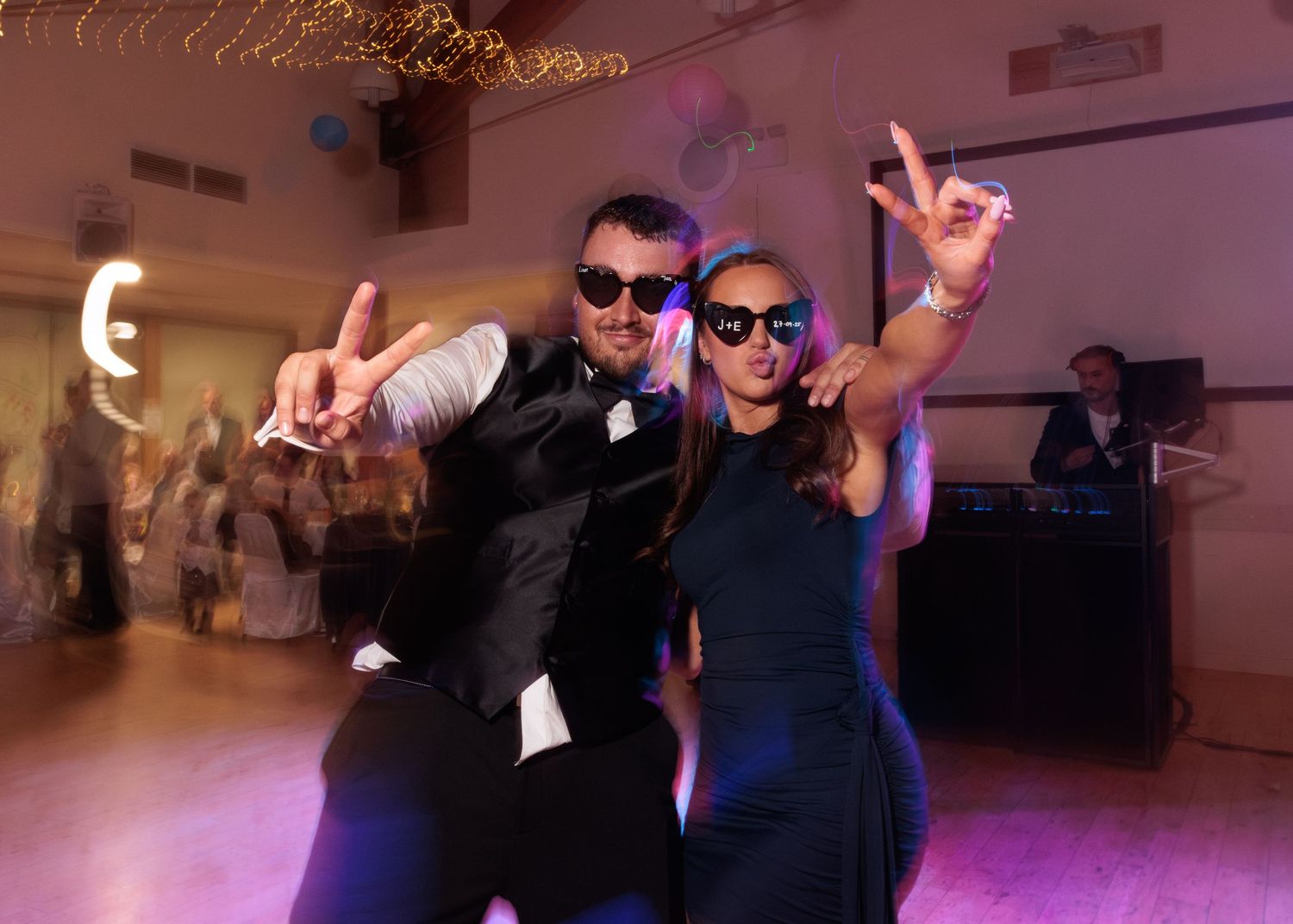 Party guests dancing energetically on a purple-lit dance floor at a wedding reception.