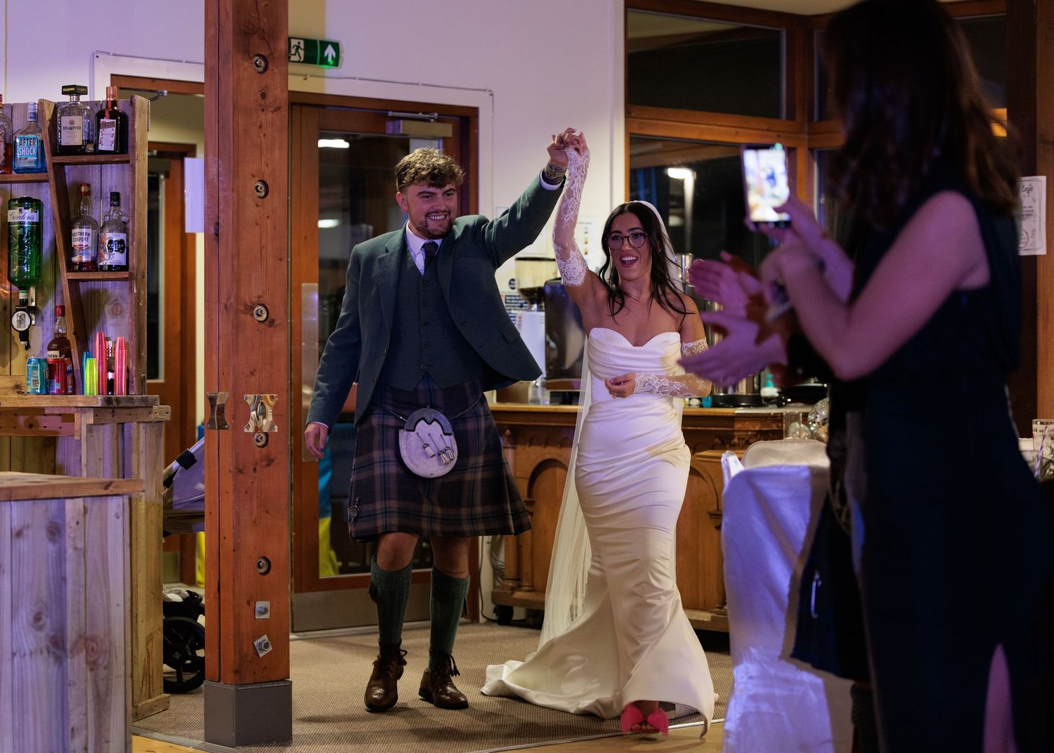 Wedding reception guests dancing and celebrating in a banquet hall with wooden beams and festive lighting.