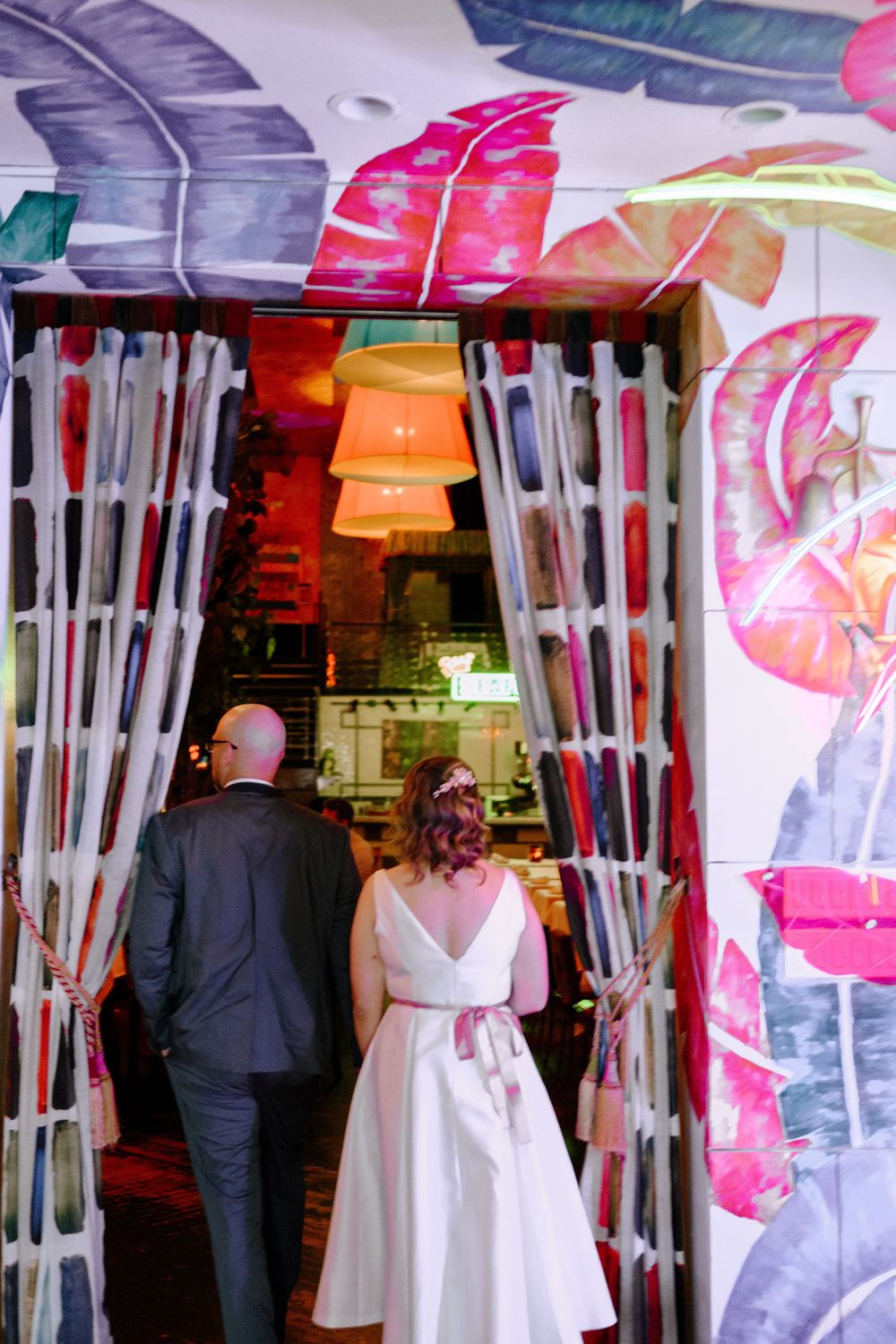 Wedding guests mingle under colorful lantern decorations and white curtain dividers at an indoor reception venue.