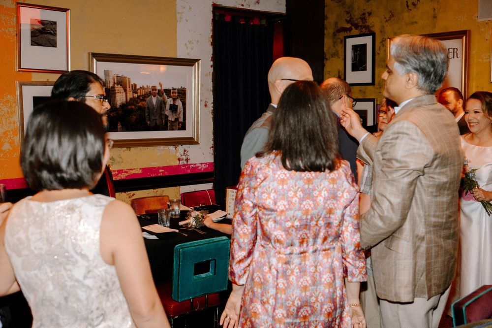 A group of people socializing and mingling at a formal event in a room with framed artwork on the walls.