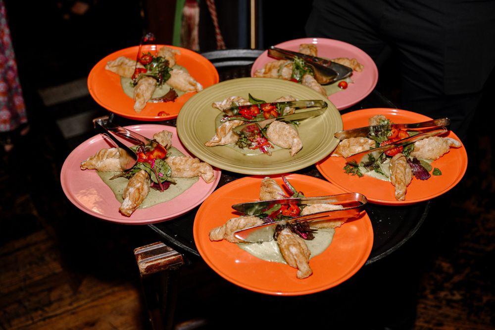 Sushi rolls and sashimi served on vibrant orange and pink plates arranged across a dark wooden table.