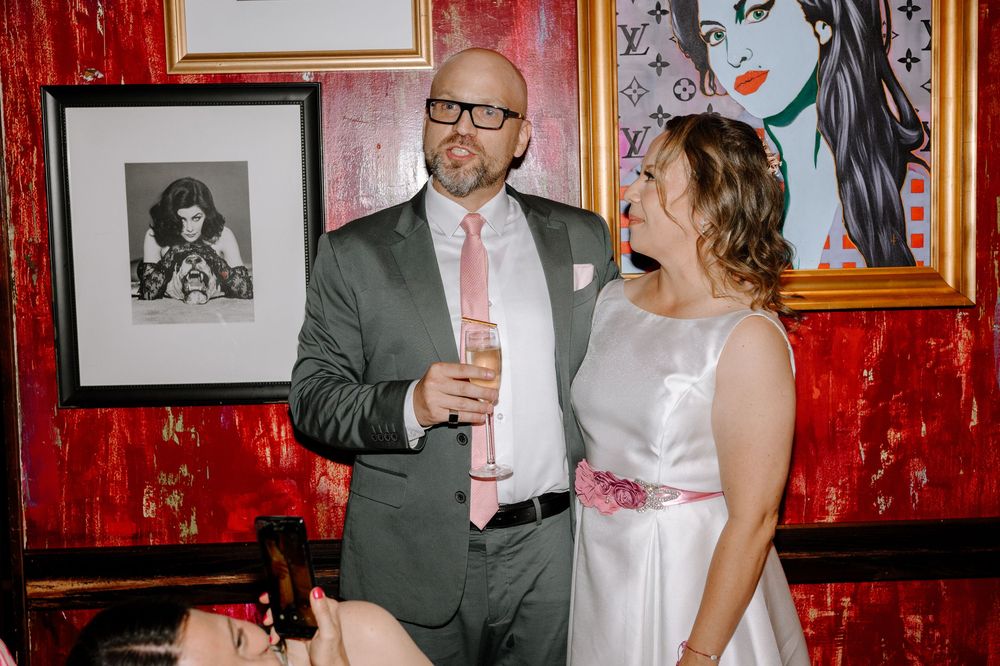 Wedding guests celebrate and dance together at a reception with red walls and framed photos in the background.