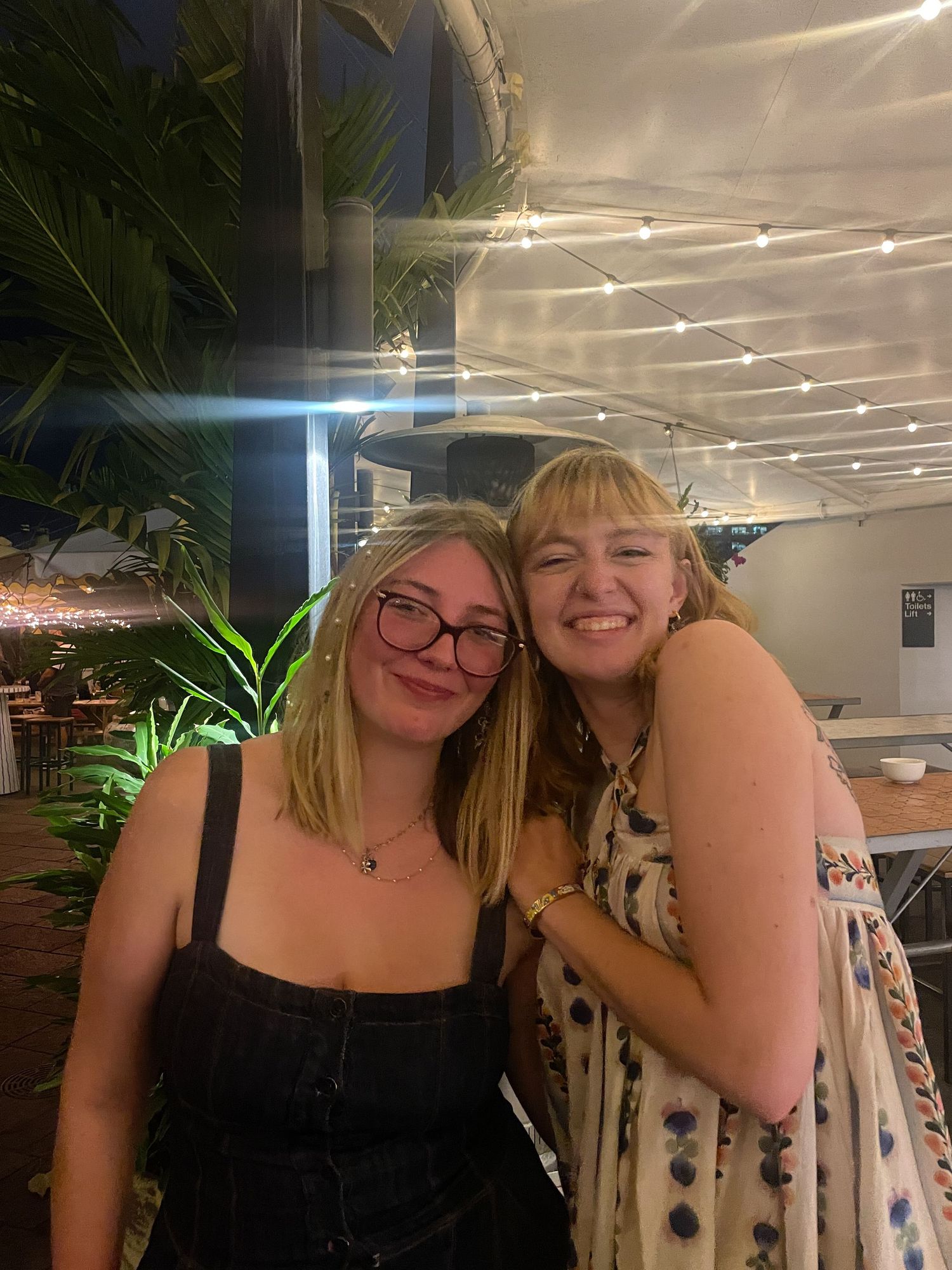 Two friends enjoying a night out at a restaurant with indoor plants and modern lighting.