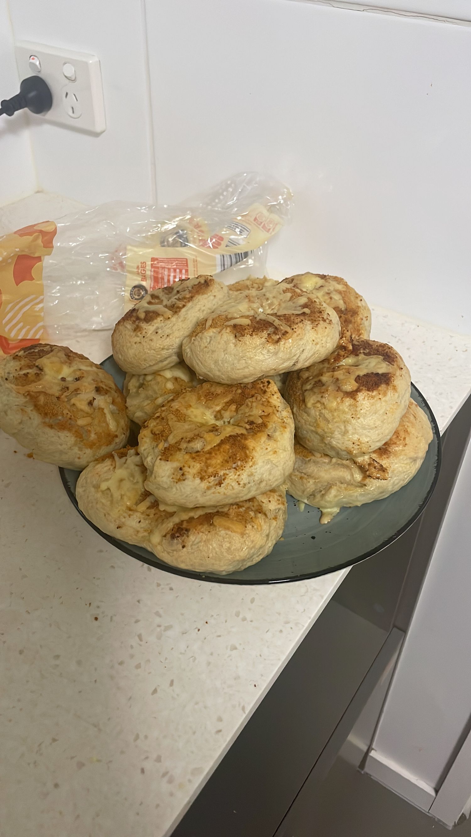 A plate of freshly baked golden brown bagels arranged on a glass plate against a white counter surface.