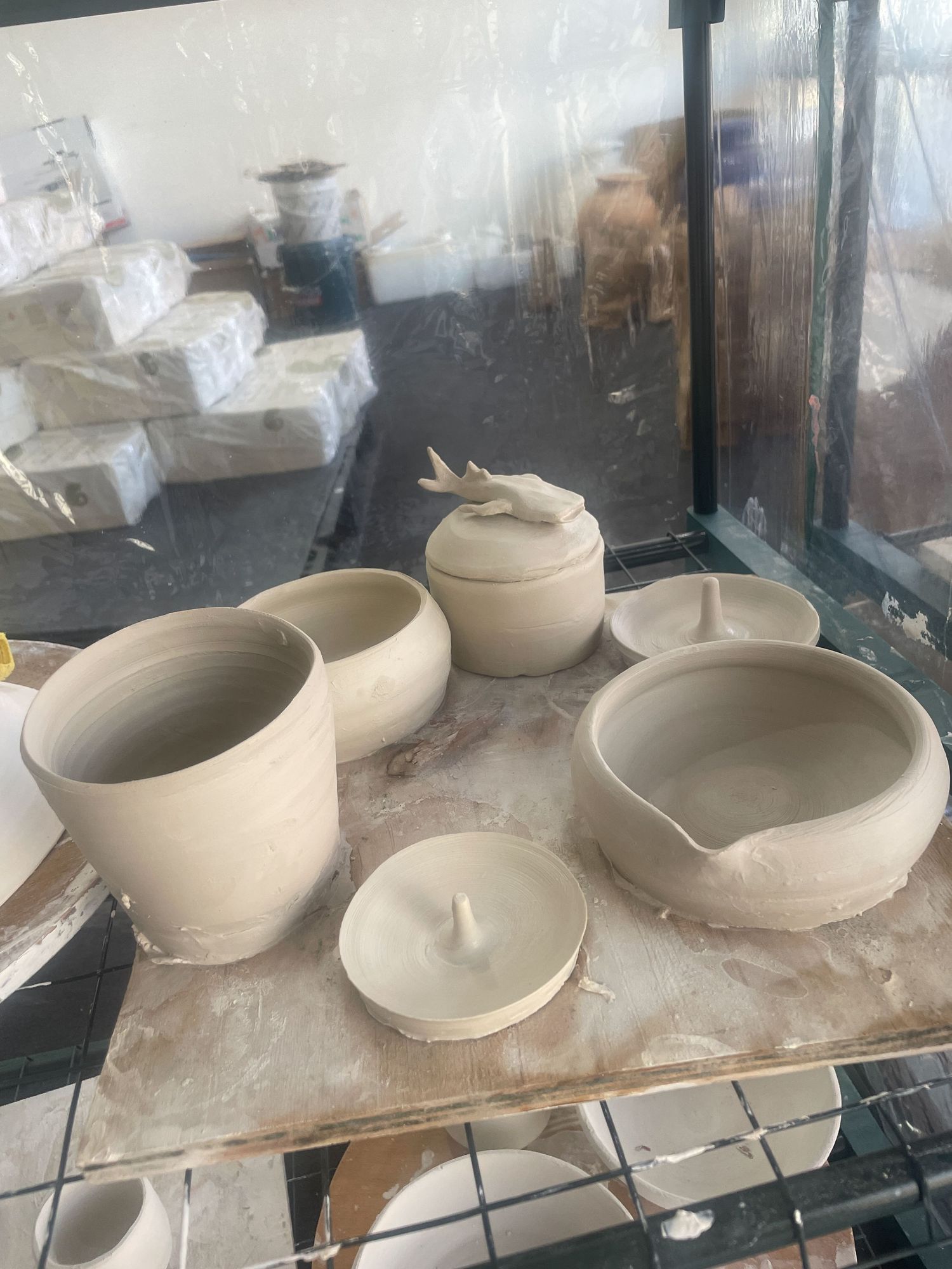 Handcrafted ceramic bowls in various stages of completion sit on a dusty pottery workshop table.