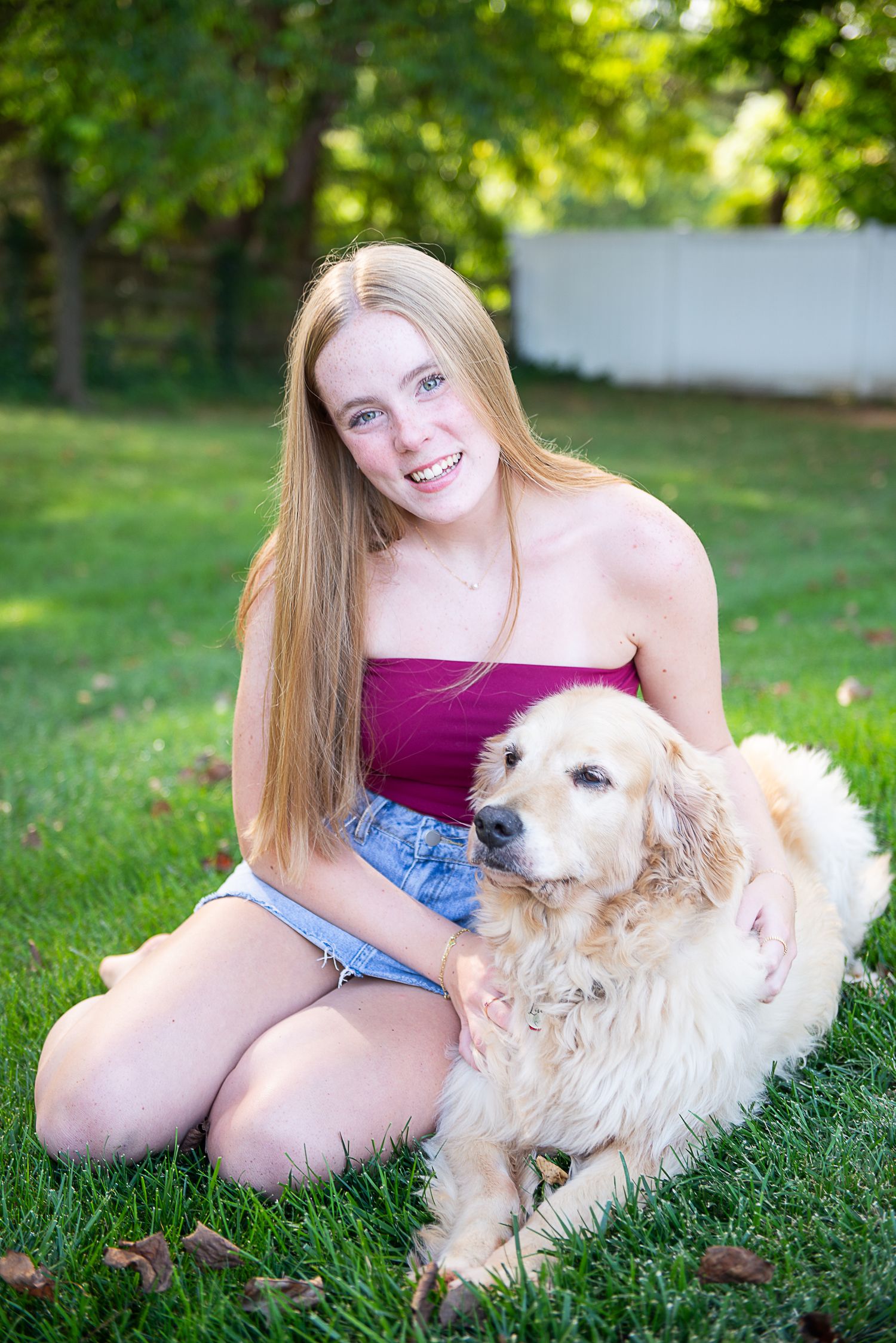 A fluffy golden retriever mix dog relaxes on green grass while being petted on a sunny summer day.