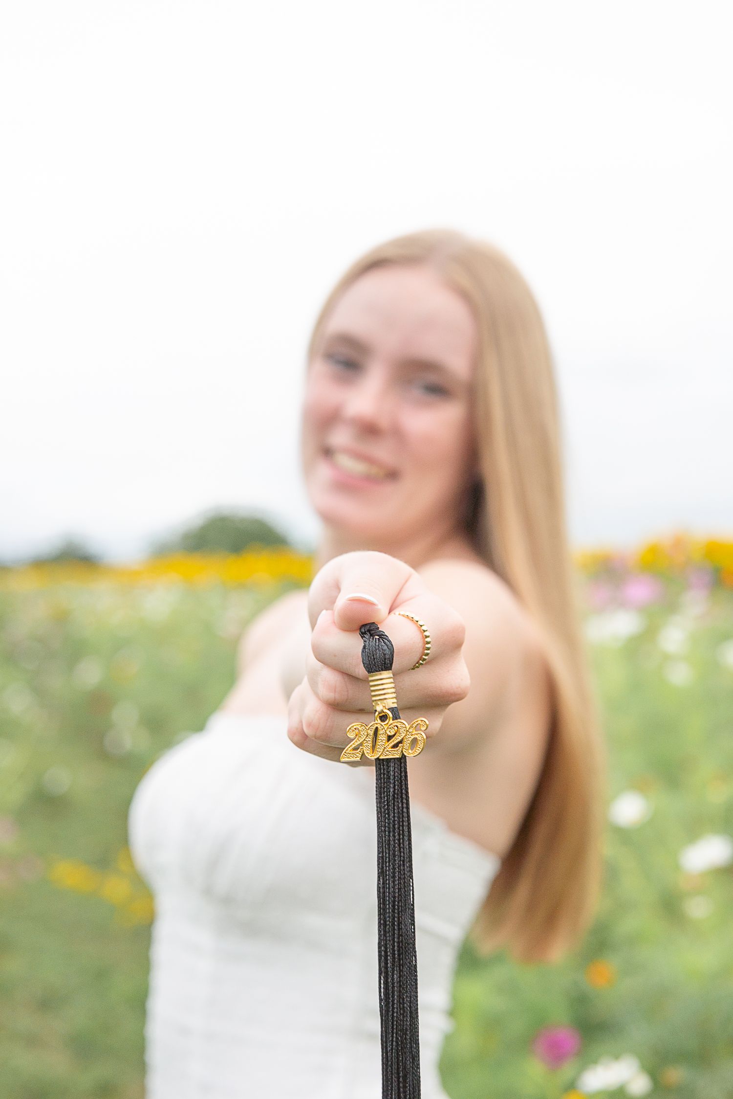 A person holds up a black tassel decoration against a blurred floral garden background.