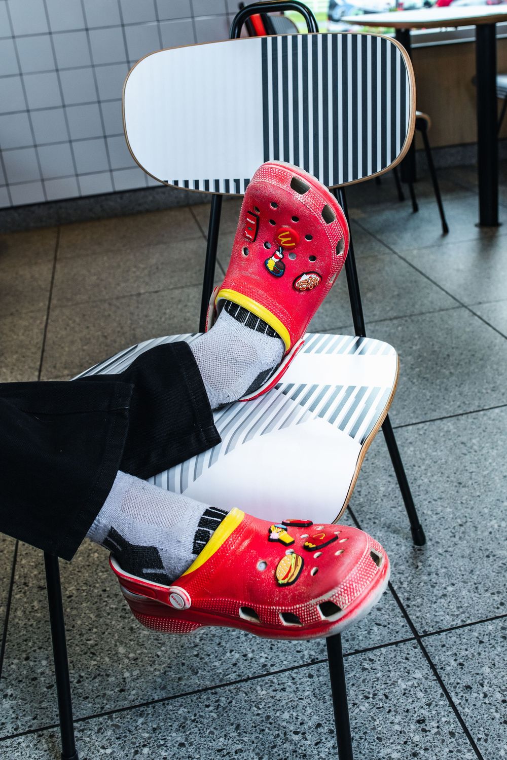 Red and white basketball shoes with cartoon designs displayed on a tiled floor near black chairs.