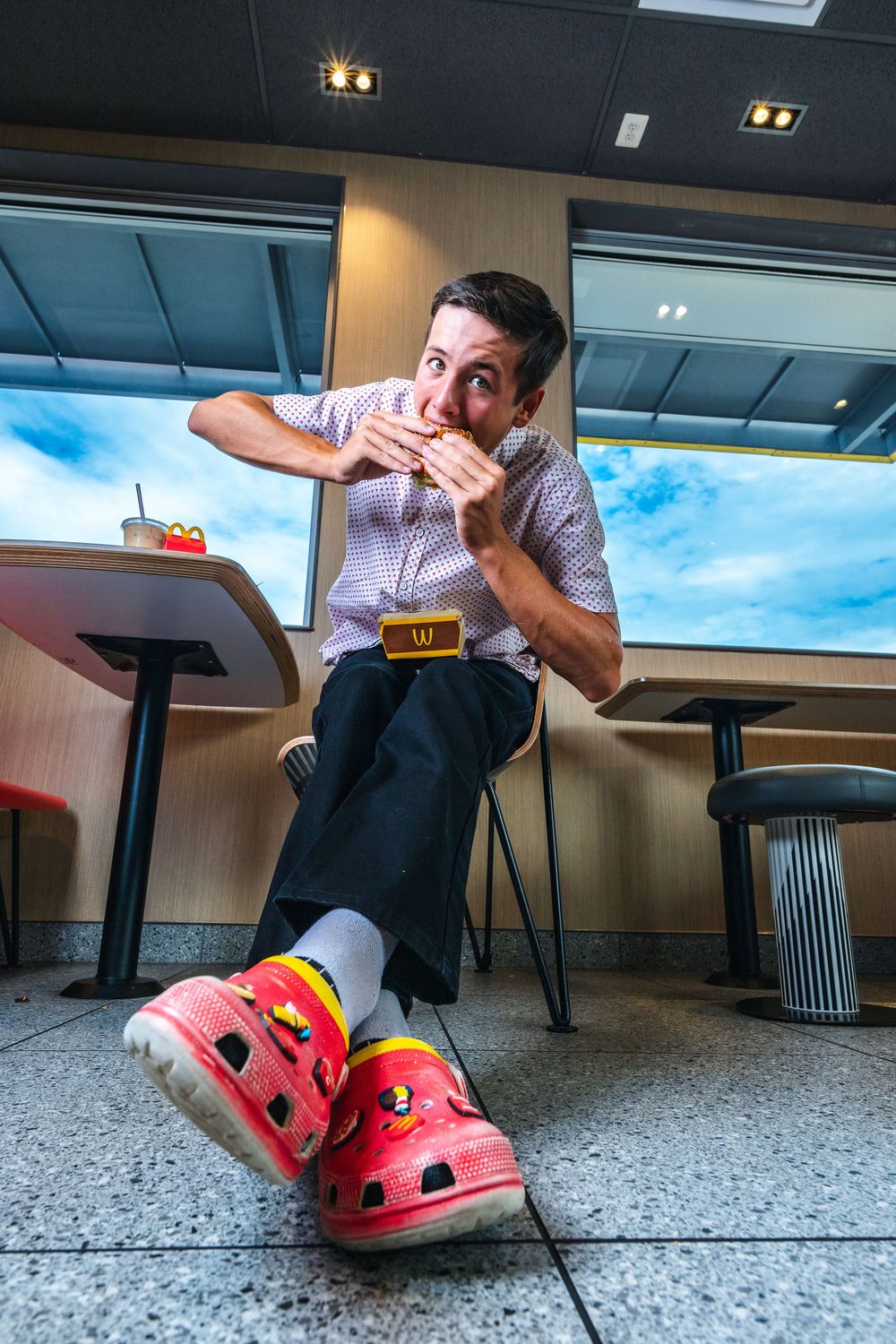 A person in red crocs shoes poses playfully on the floor of an office space with a window view.