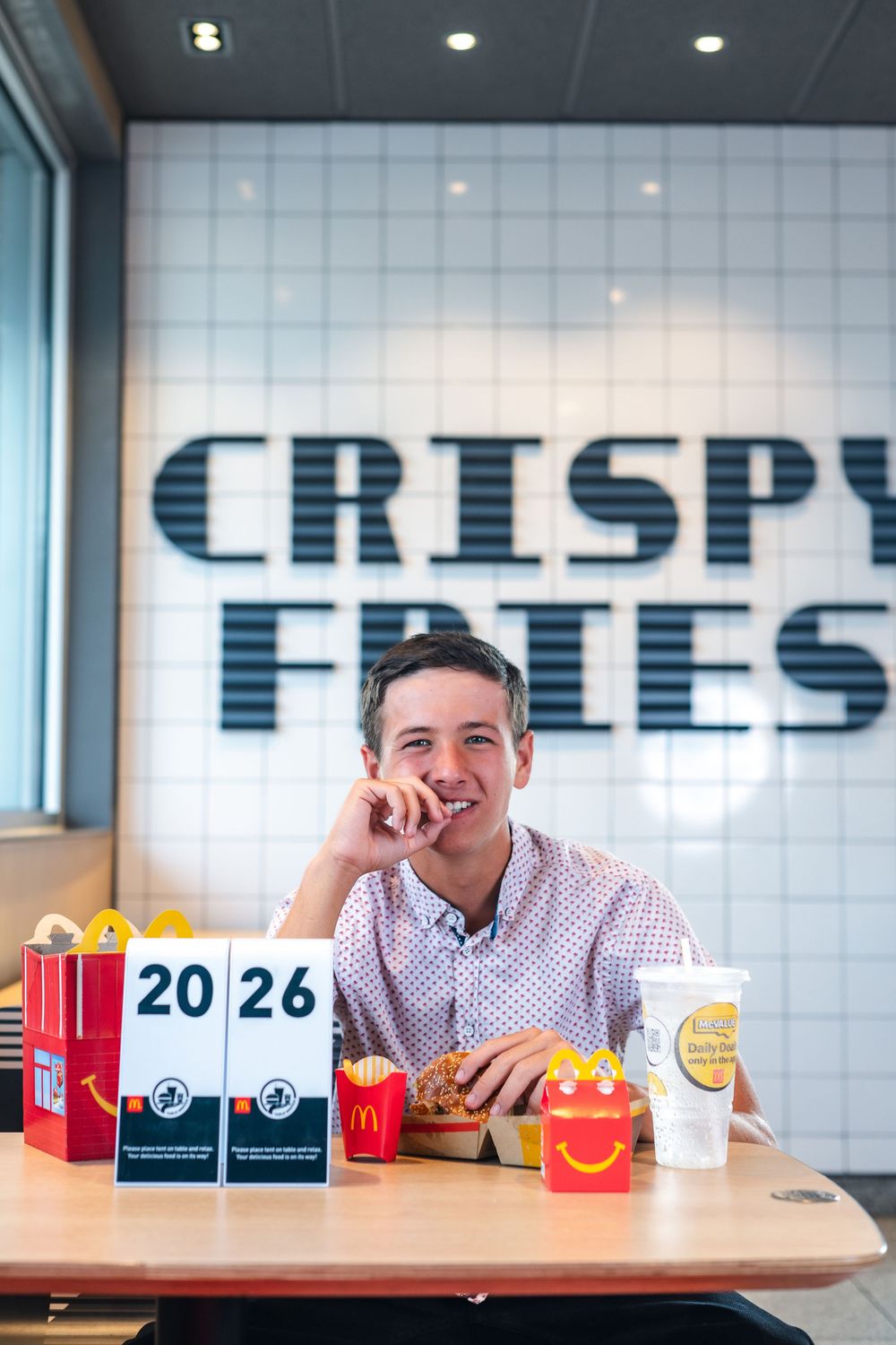 A customer enjoys a meal at McDonald's with crispy fries signage visible, surrounded by food items and packaging.