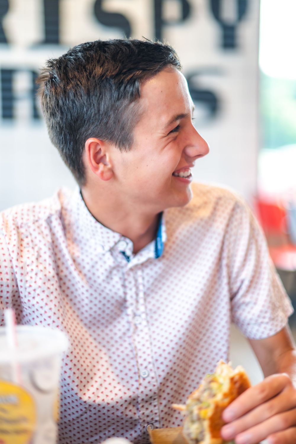Person in polka dot shirt smiling and enjoying a meal at a restaurant.