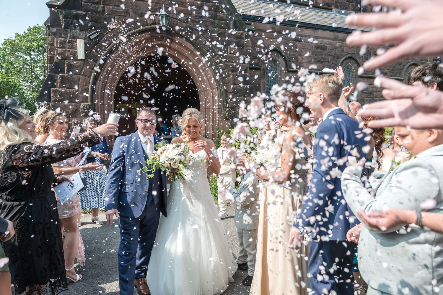 Wedding guests shower newlyweds with white confetti as they exit the ceremony in a joyous celebration.