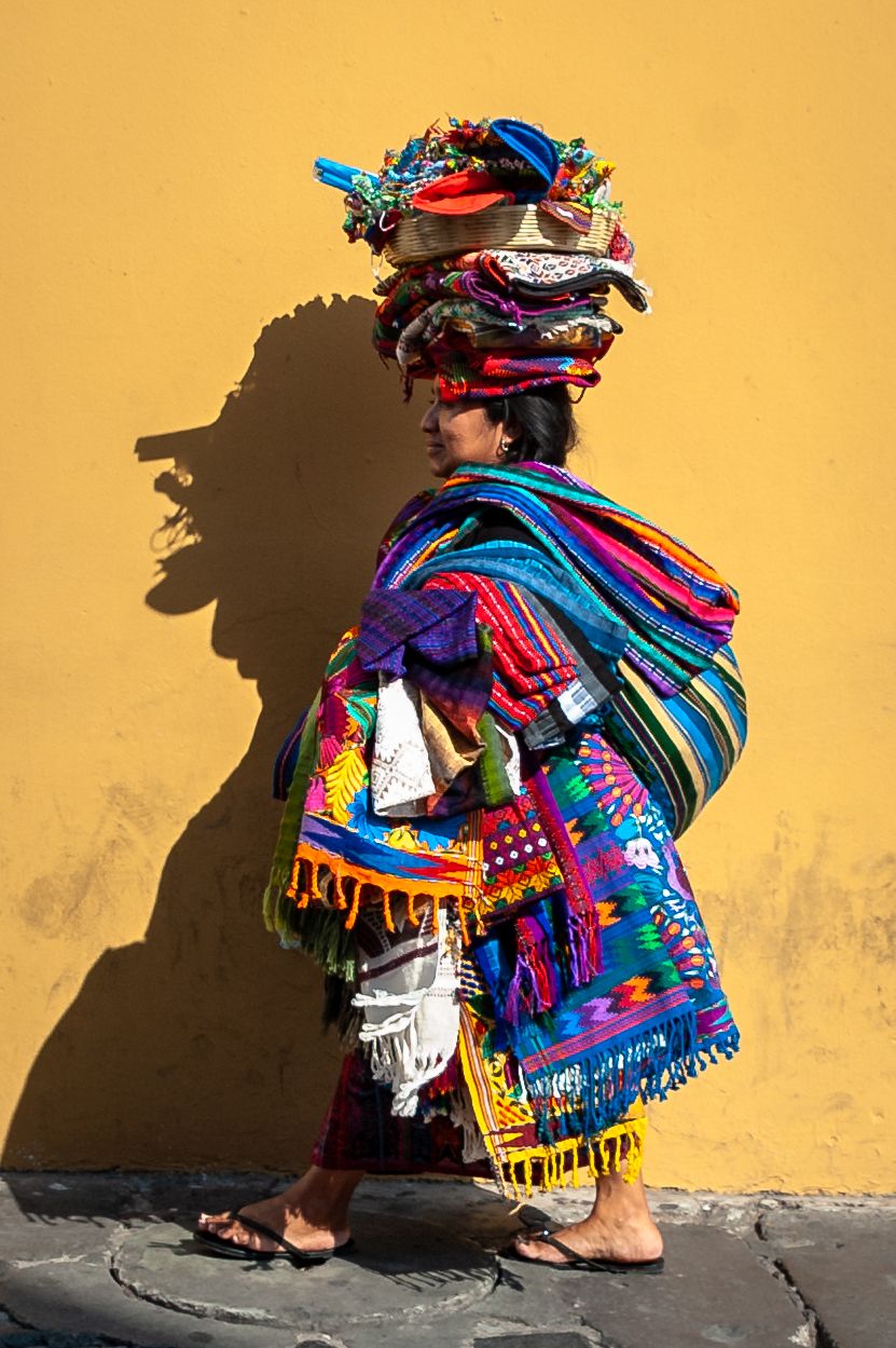 Colorful traditional Peruvian textile vendor sits against yellow wall casting dramatic shadow in sequence of images.