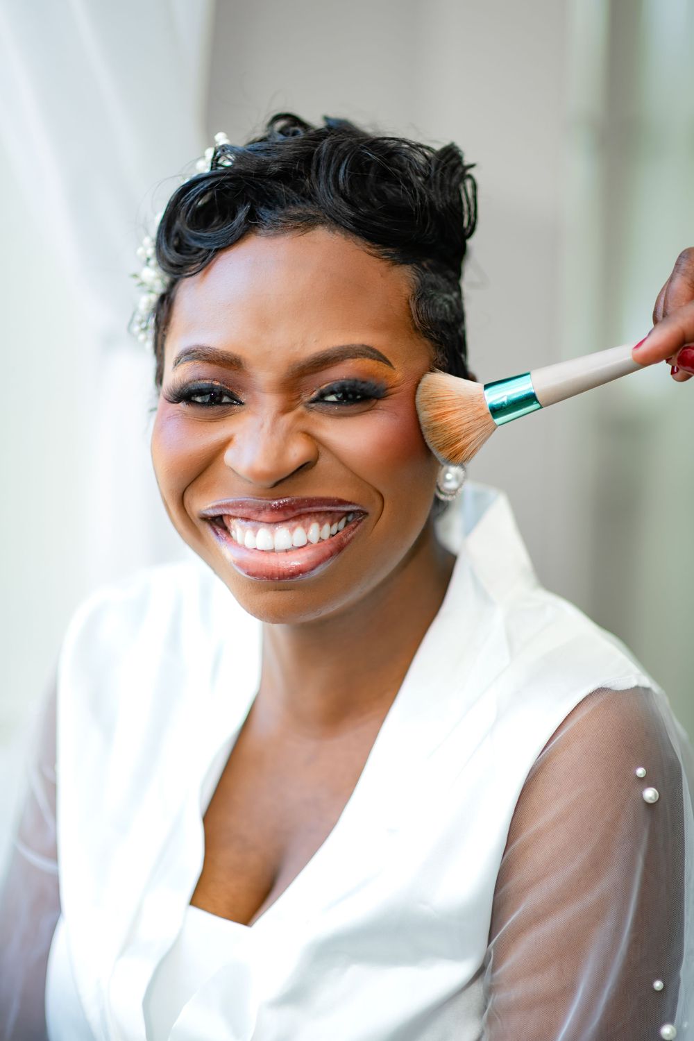 Makeup artist applies powder with a fluffy brush during bridal beauty preparation in a white robe.