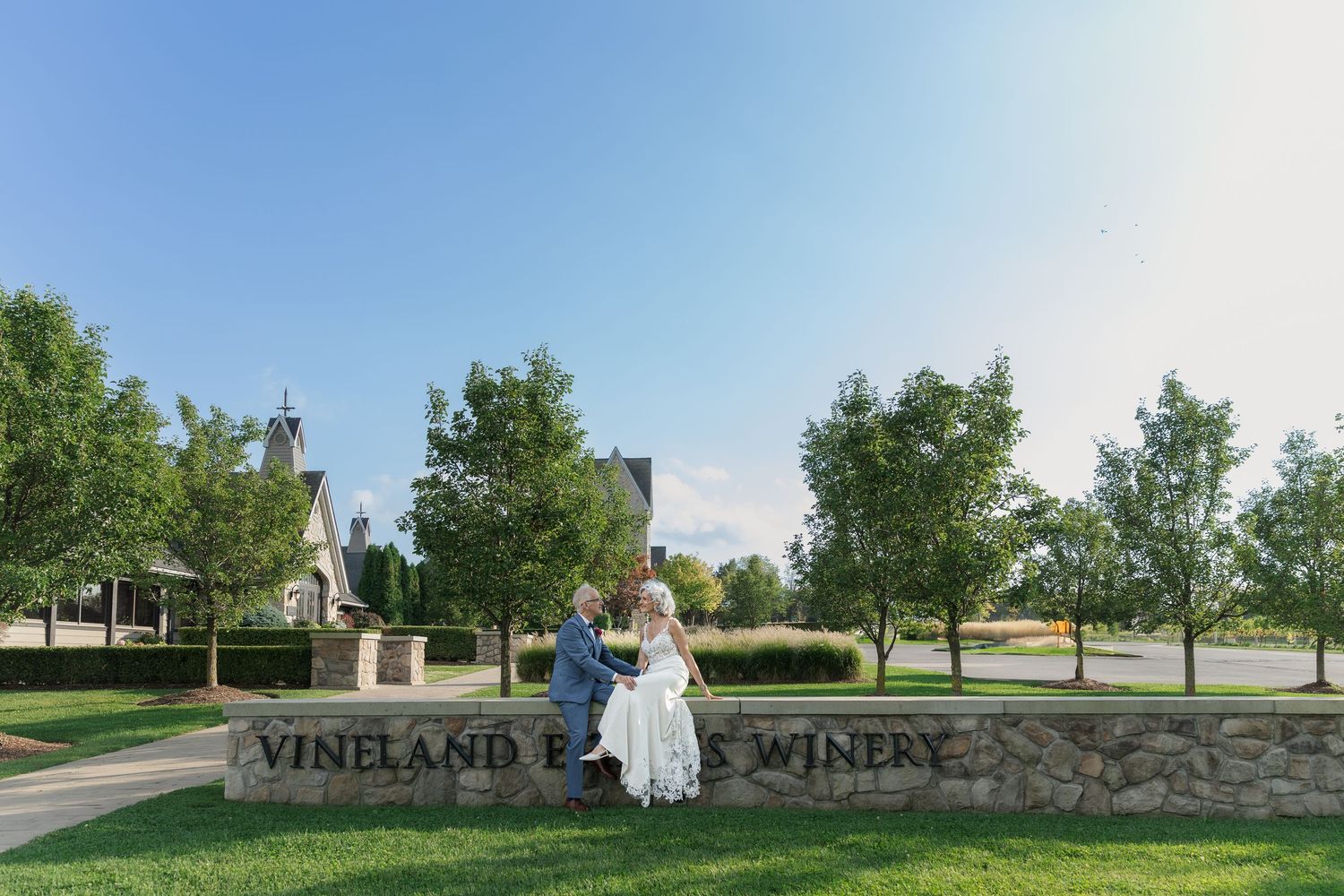 Bride and groom enjoy a moment together sitting on the stone wall entrance at Vineland Estates Winery.