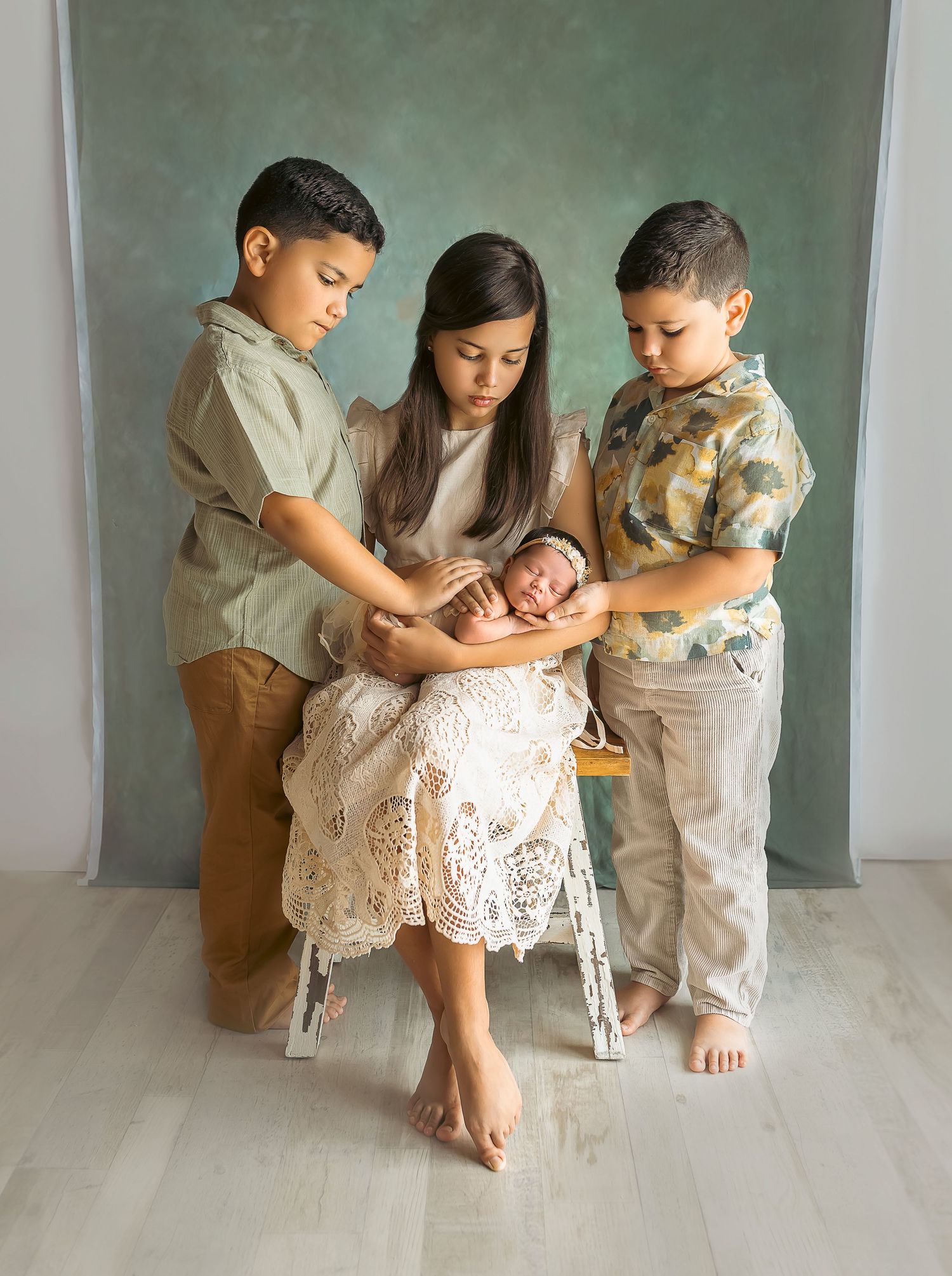 Tres ninos aguantan una bebe recien nacida. Su nueva hermanita, mirandola. Child Photographer. Baby Photoshoot.