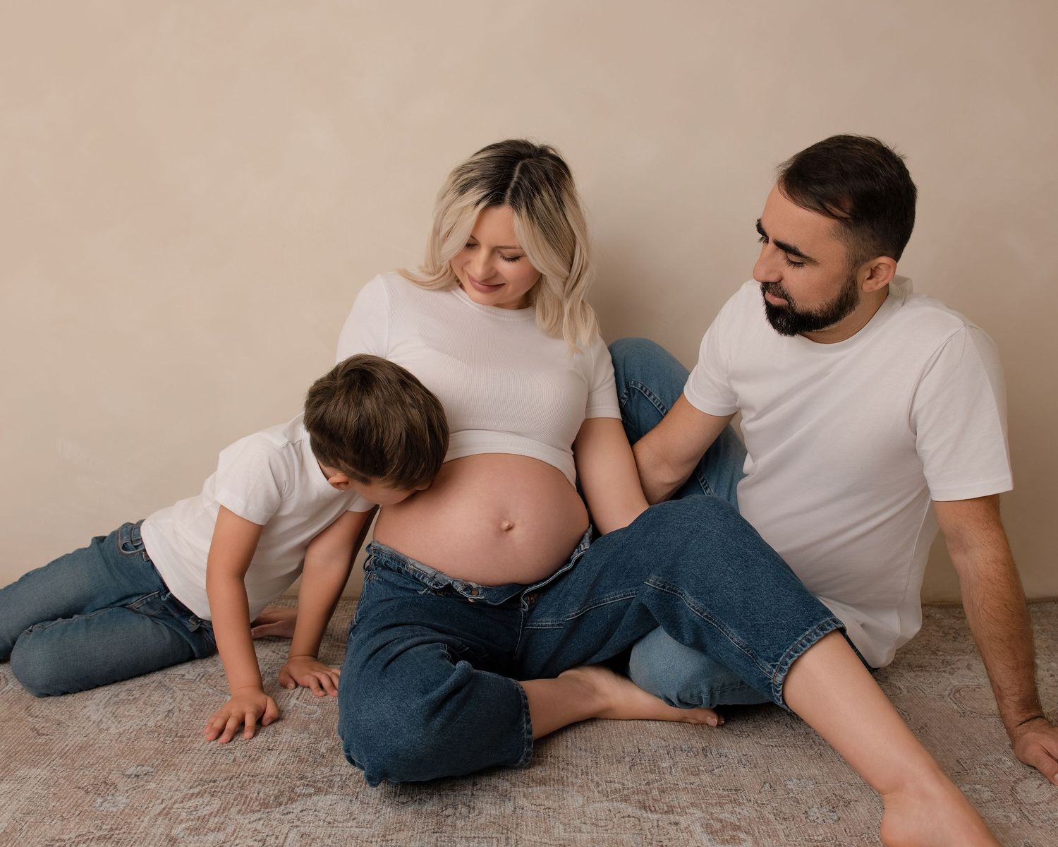 Sibling kissing mum's pregnant baby bump in a relaxed maternity photography session.