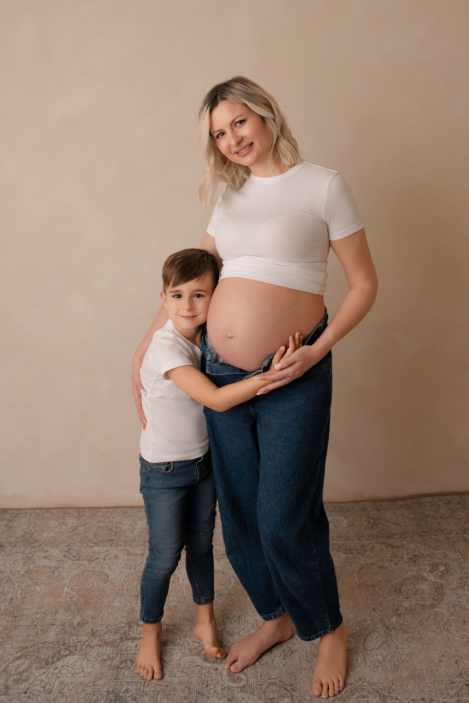 A series of tender moments showing a young child embracing a pregnant belly while both wear white tops and blue jeans.