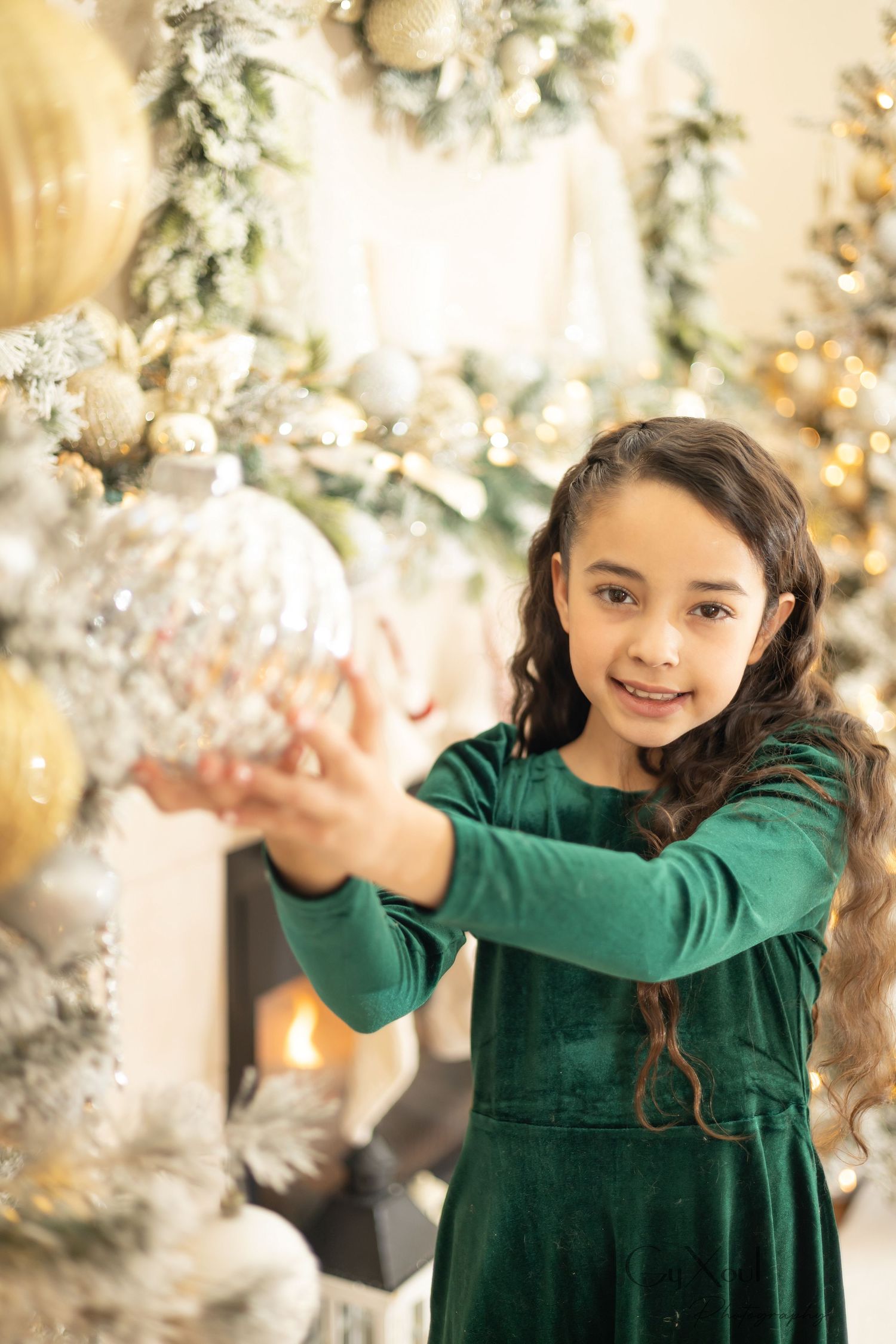 Holiday photoshoot setup with white bedding and decorative wreaths on wall in cozy bedroom setting.