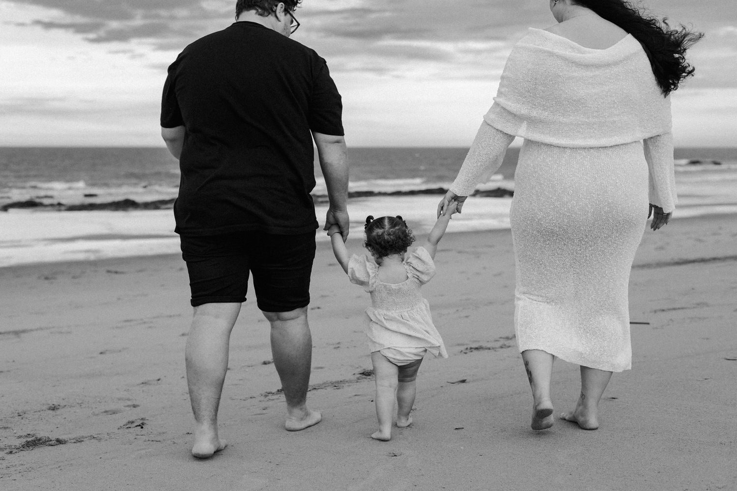 Black and white photo of people walking together on tannum sands beach holding hands.