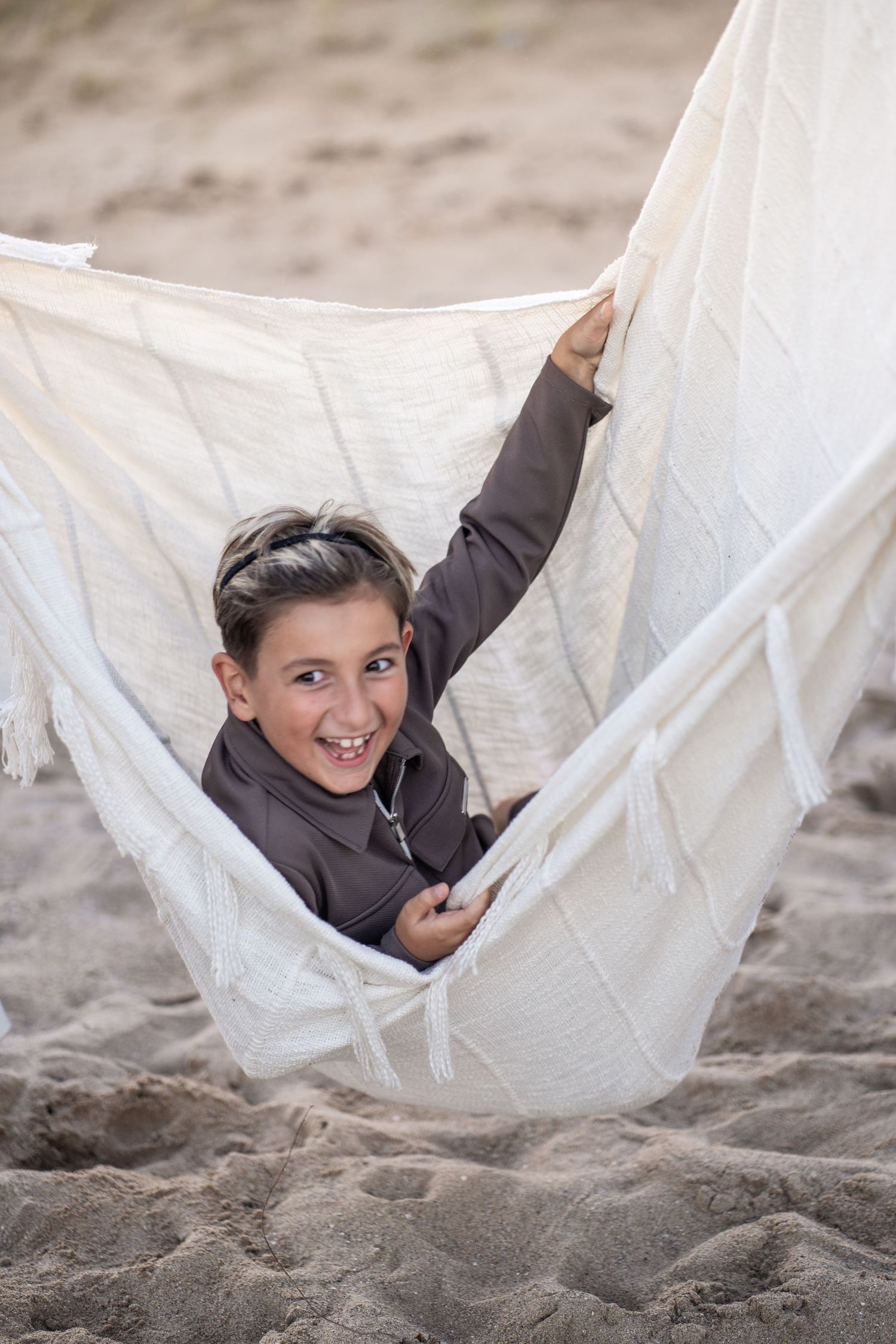 A series of photos shows someone playfully rolling and having fun in a white hammock on a sandy beach.