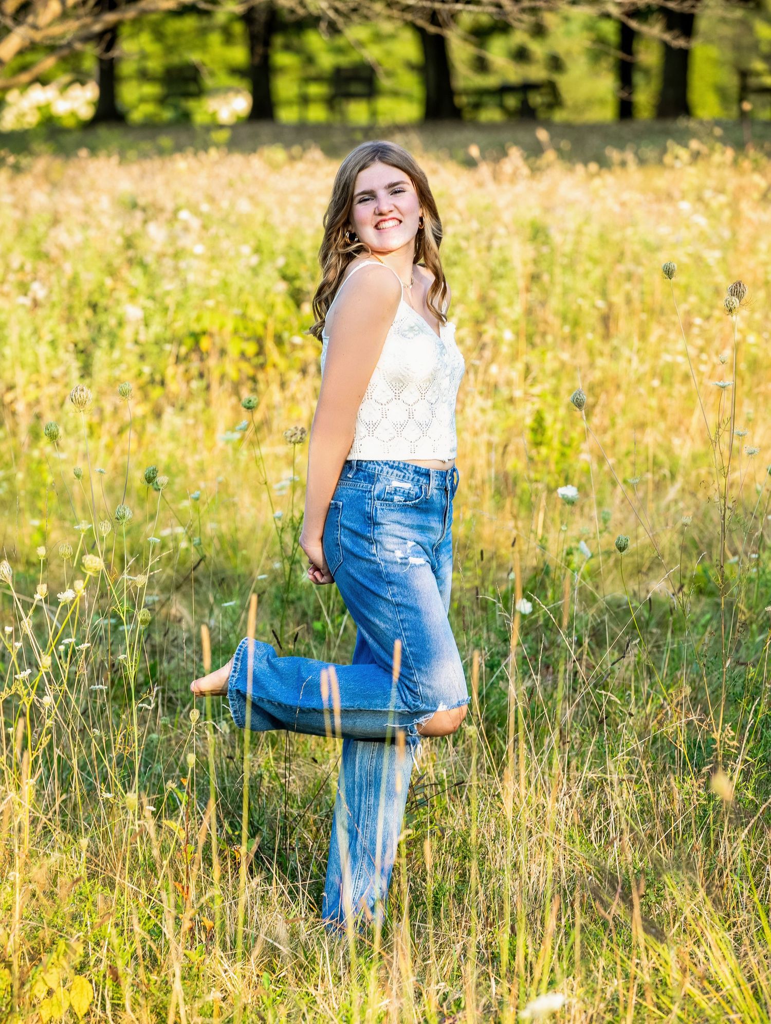 A person in denim overalls stands in a sunlit meadow of tall grass and wildflowers during golden hour.