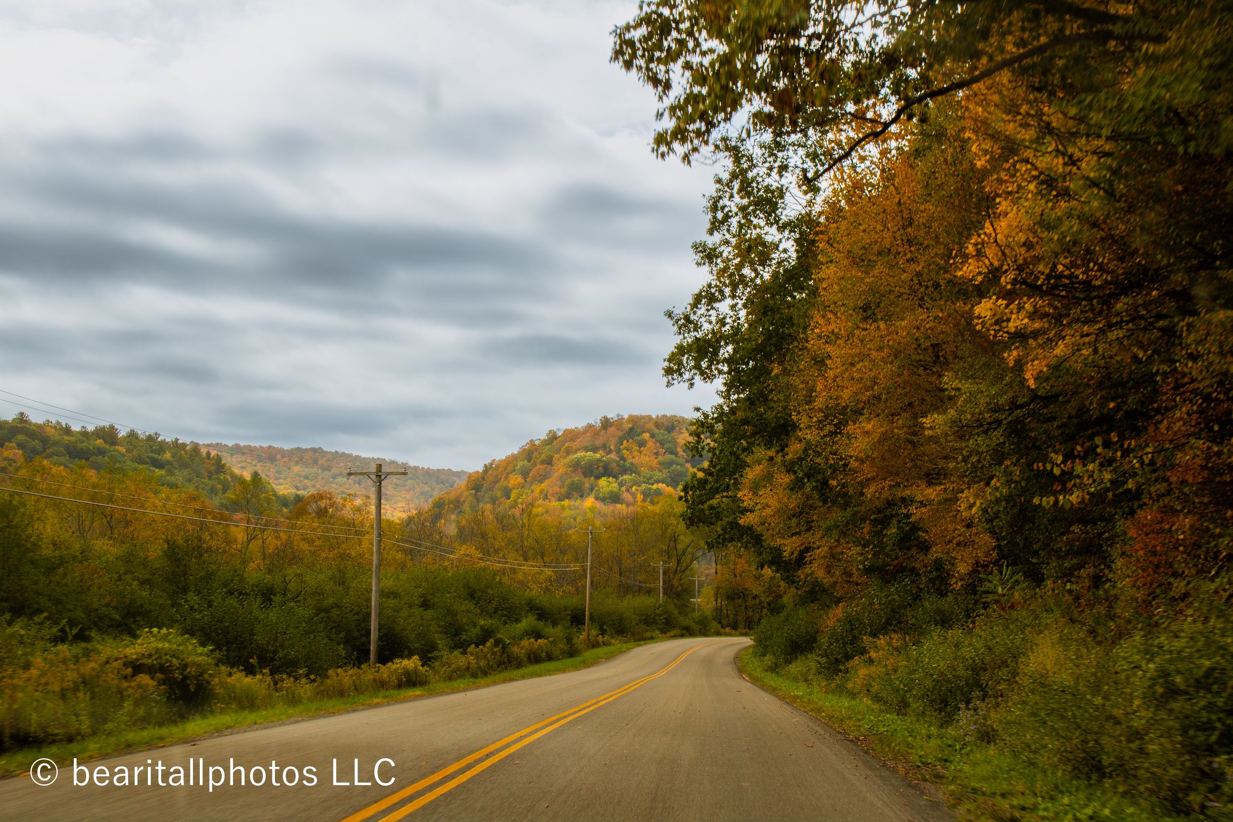 Winding country road through vibrant fall foliage with overcast sky above.