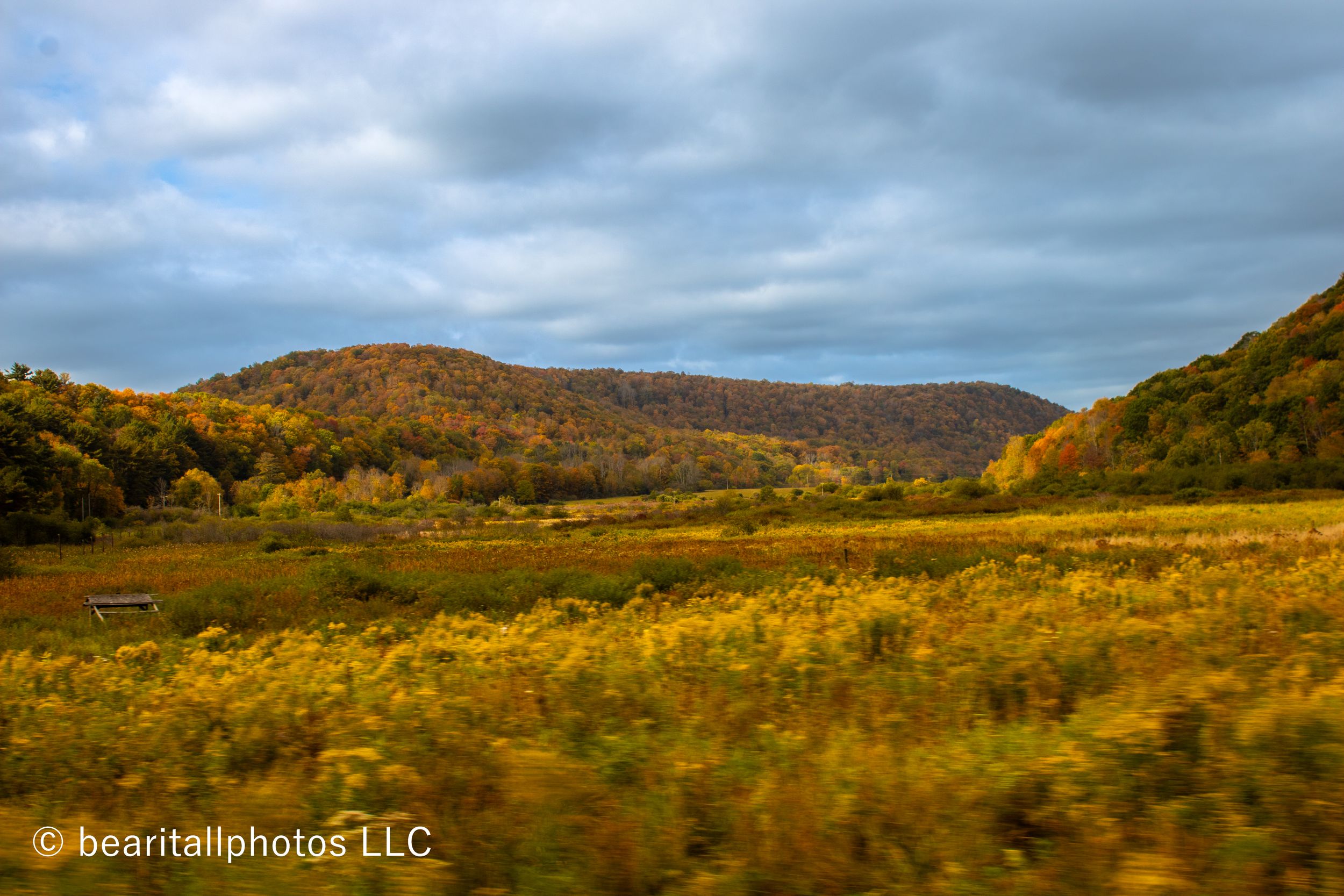 Rolling autumn hills with golden meadows under dramatic cloudy skies in rural countryside.