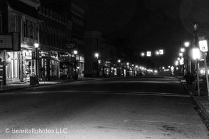 Dark urban street scene with storefronts illuminated by street lamps at night.