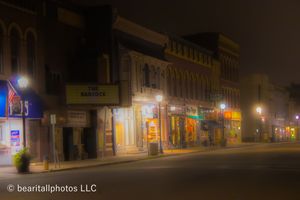 Historic downtown buildings lit up at night with warm glowing storefronts and street lights.