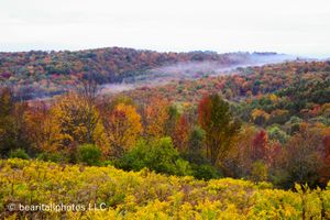 Sweeping vista of fall-colored hills and valleys shrouded in morning mist.