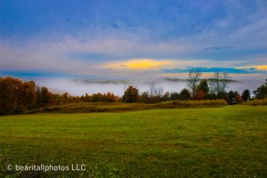 Wide panoramic view of green meadows and distant hills beneath a dramatic cloudy sky.