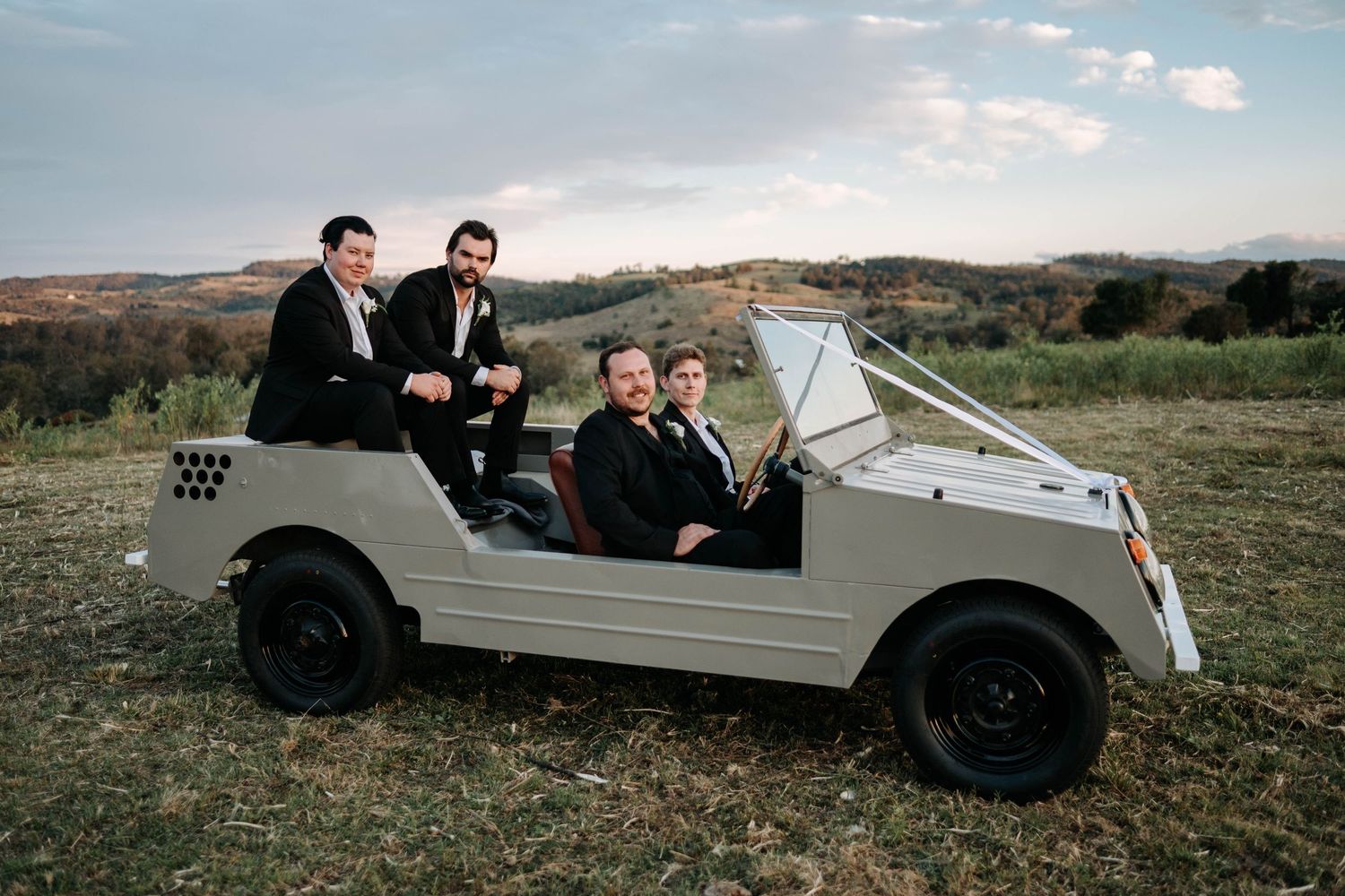 A white vintage car parked in a grassy field with rolling hills in the background.