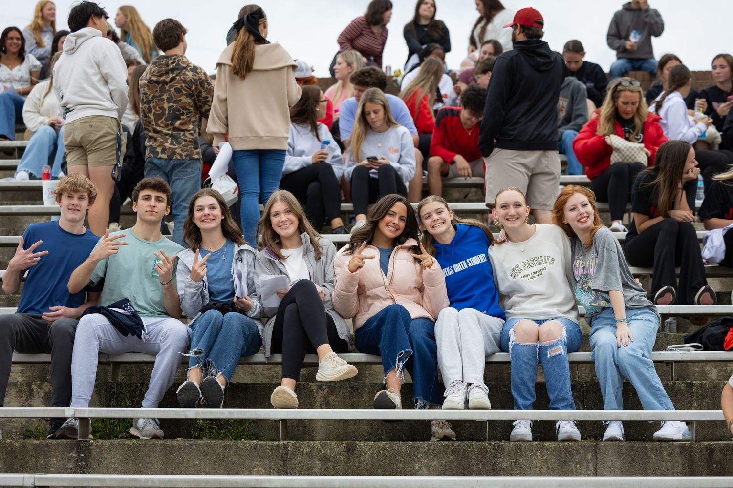 Group of students sitting together on outdoor bleachers while socializing and looking at their phones.