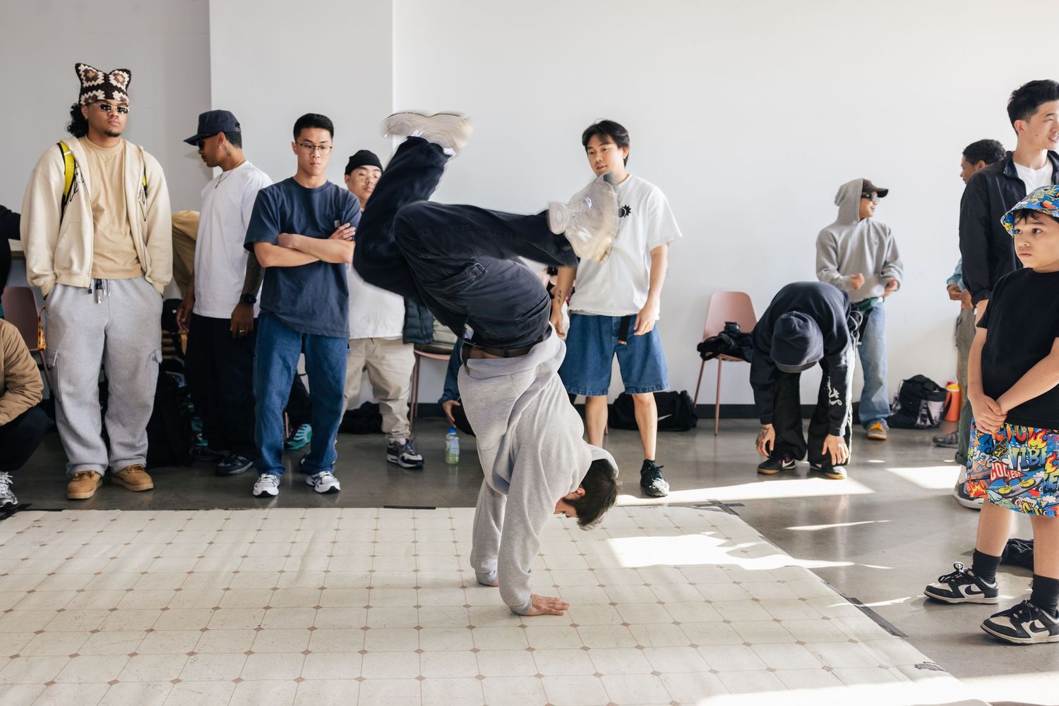 A group of people practicing skateboarding tricks indoors on a smooth floor in a minimalist space.