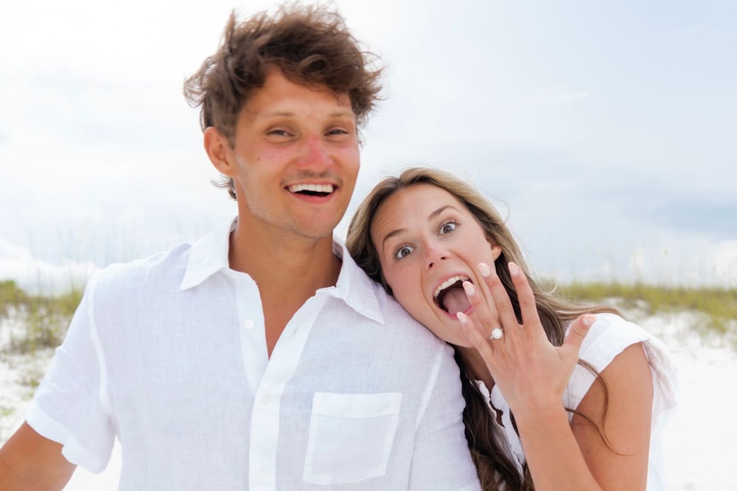 A couple in white clothing shares joyful moments together on a beach.