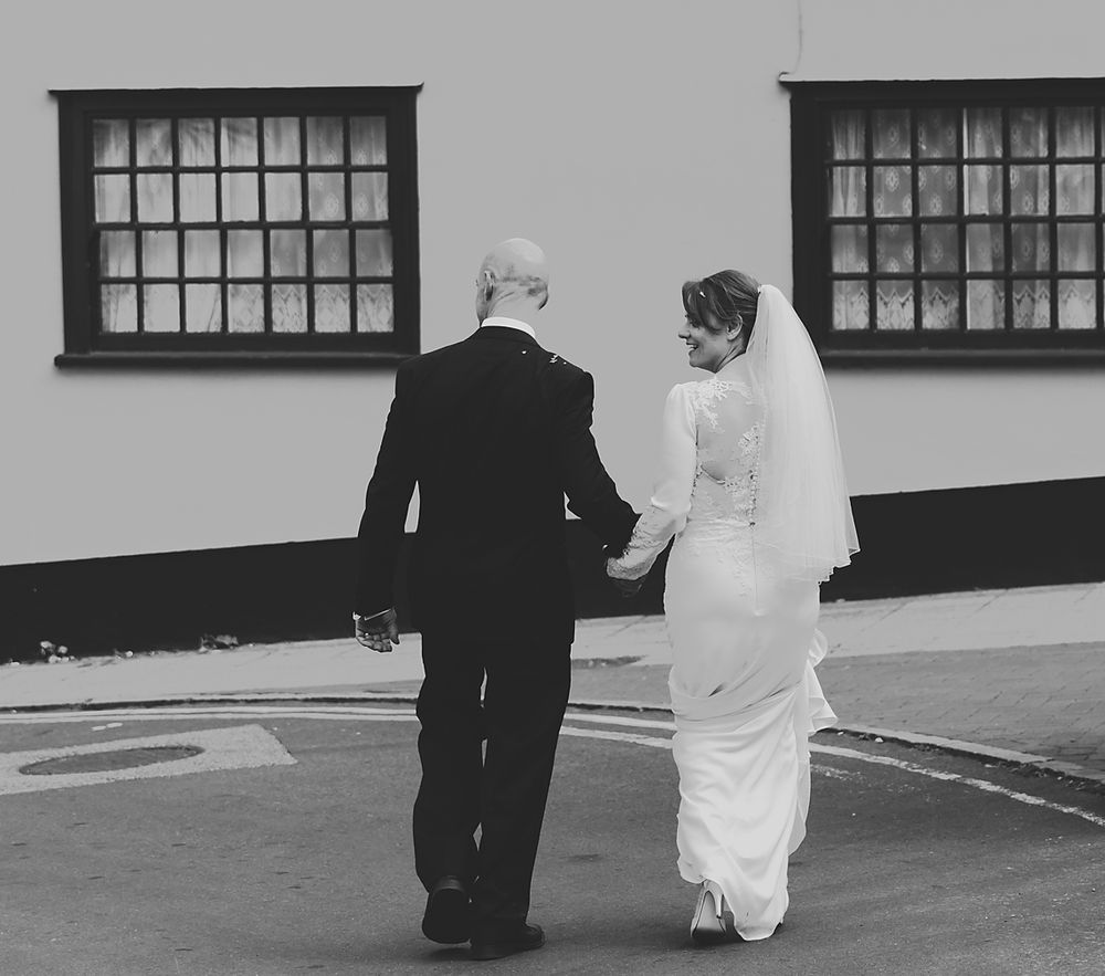A wedding couple walking hand in hand along a building with traditional windows.