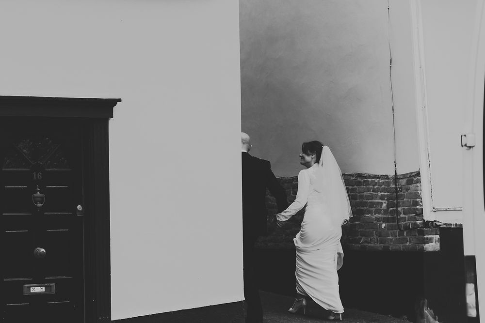 A bride in white dress walking near a doorway in a black and white photograph.
