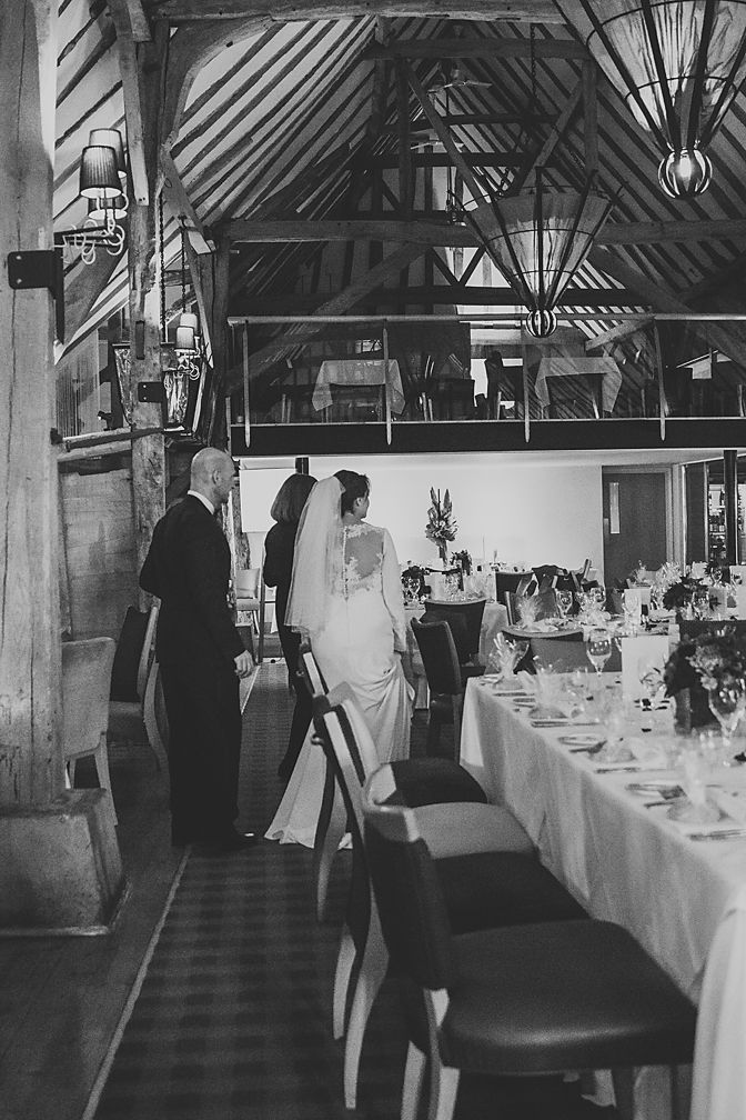 Reception venue with exposed wooden beams and decorated tables in black and white photography.