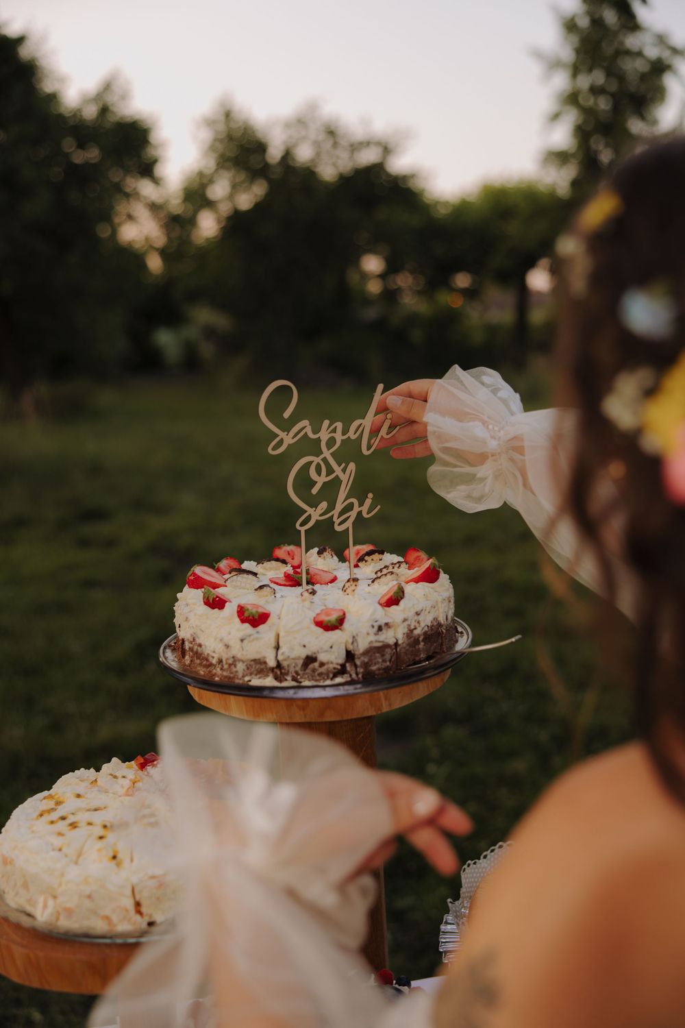 Wedding dessert table with tiered cakes and treats decorated with fresh flowers and berries at sunset.