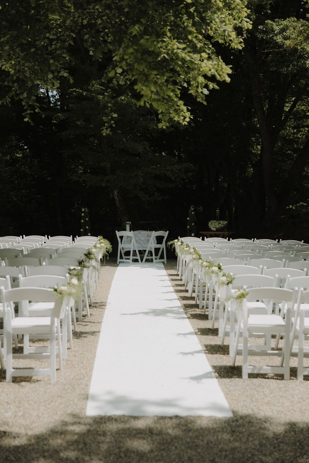 Rows of white folding chairs arranged outdoors for a garden wedding ceremony under shady trees.